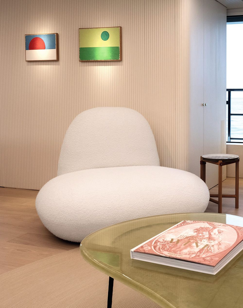 Close-up of a lounger which has a huge seat pad and is low to the ground. There are two pieces of art on the wall behind, one is blue and white with a red circle, the other is yellow and green with a green circle