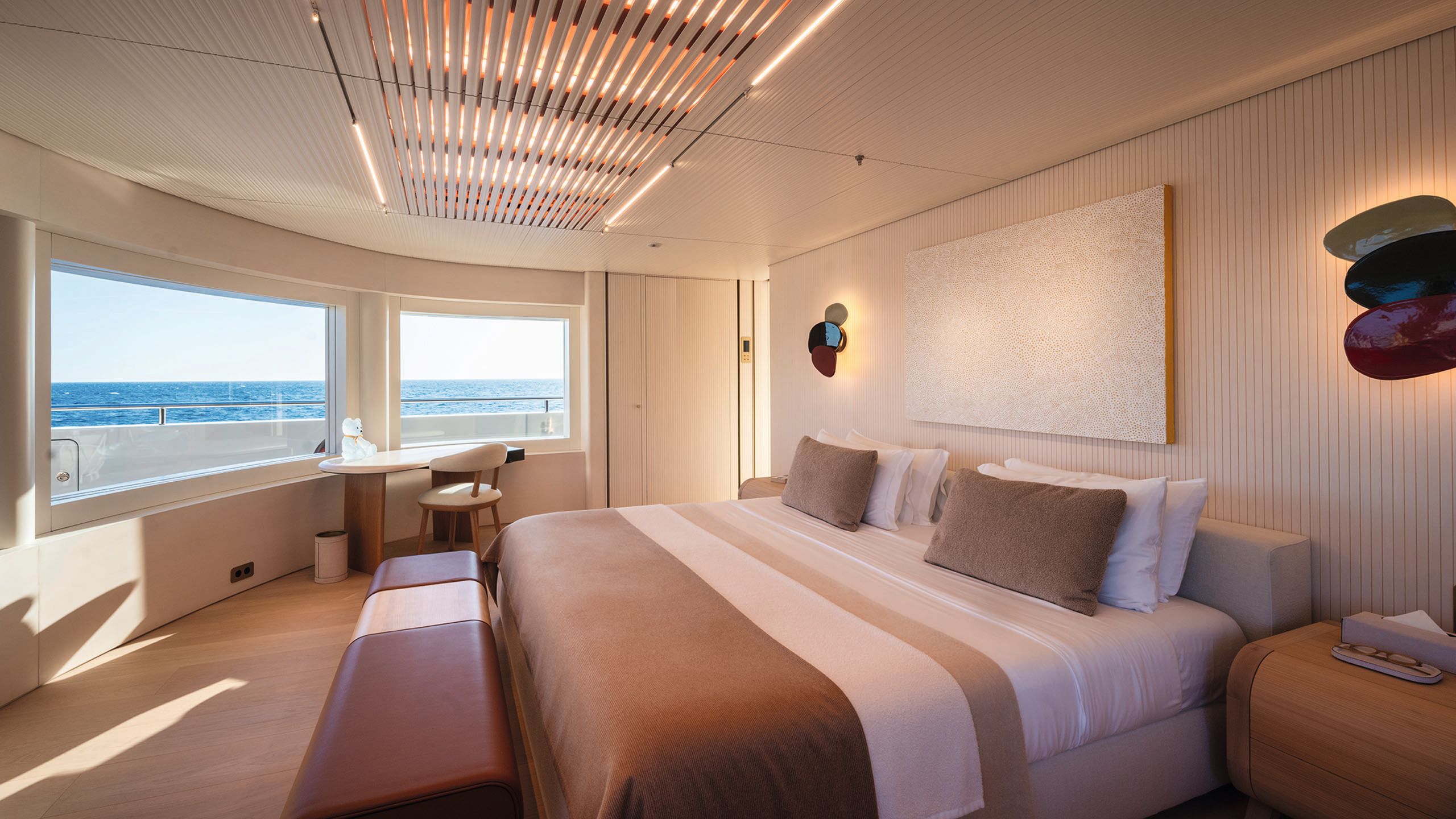 Owner's cabin with large bed at the centre made up with neutral and brown bedding. The bench in front has a dark leather top