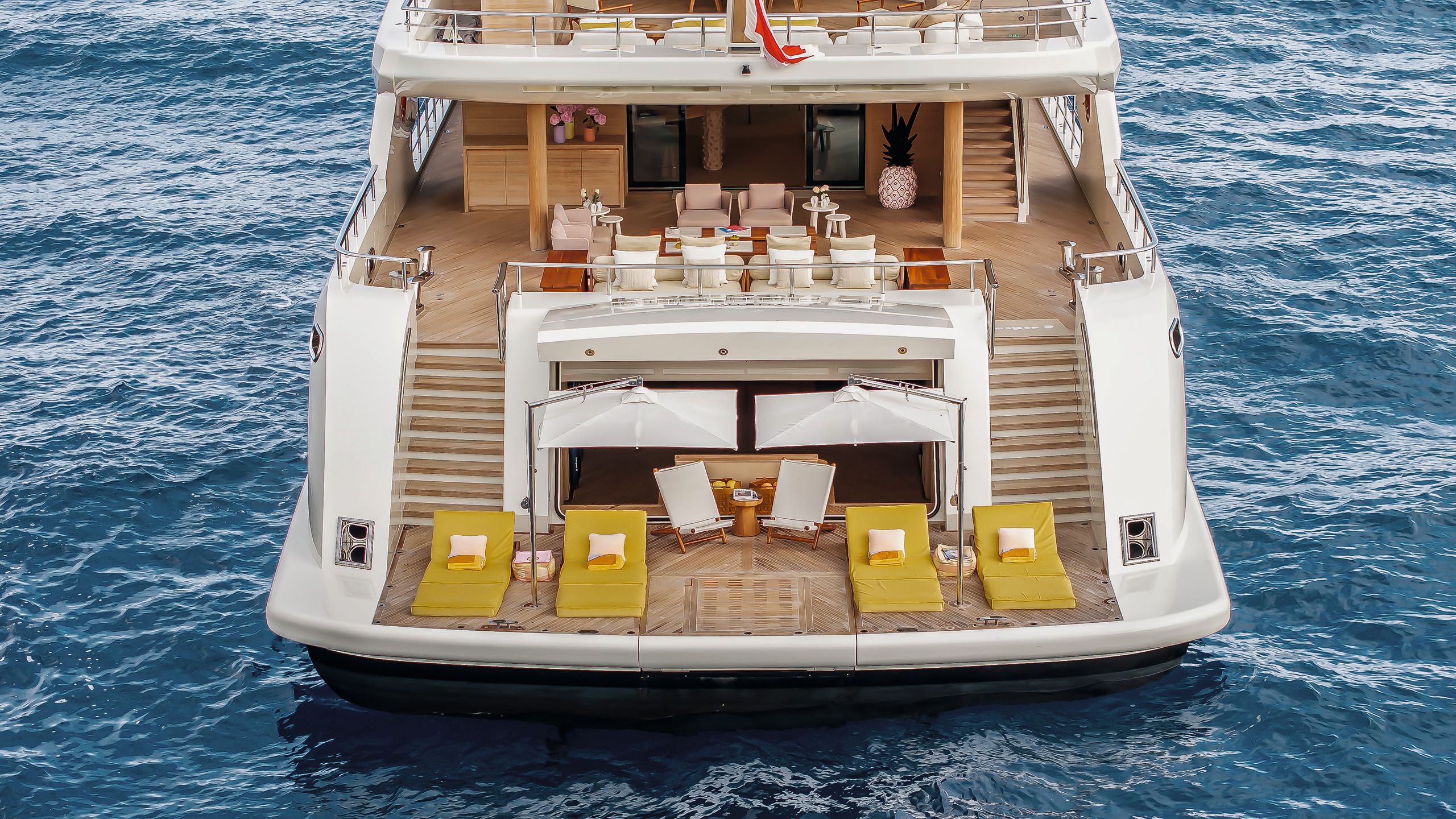 Overhead exterior view of the beach club area. There are large yellow sun loungers at the front with white parasols. Two staircases either side lead up to a deck with lounge-style sofas and chairs