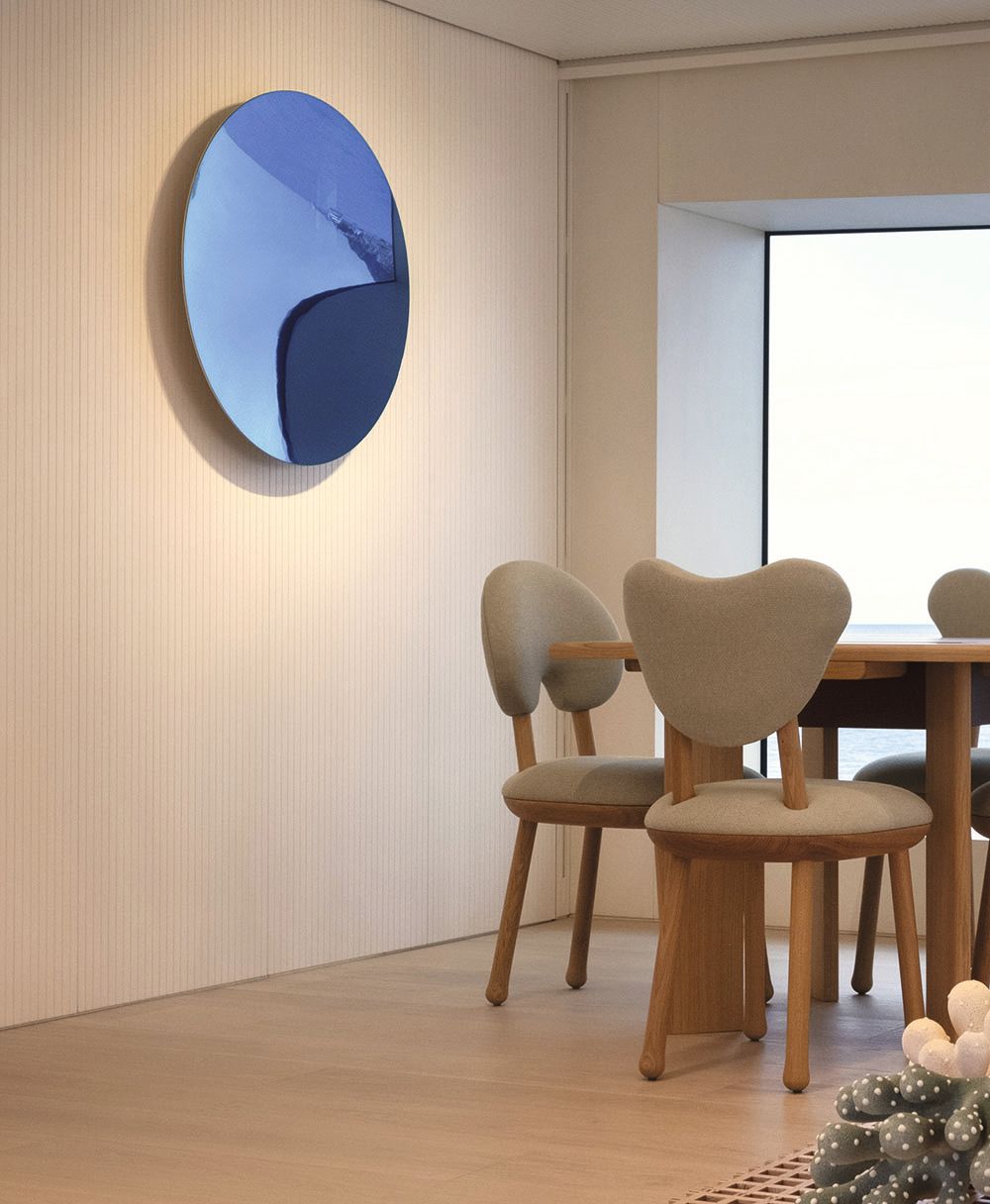 Close-up of the back of the dining chairs. A large blue circular mirror hangs on the wall