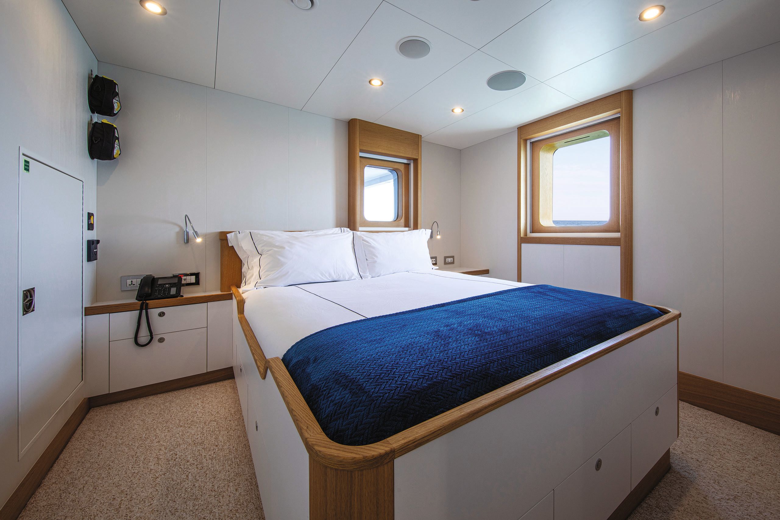 A cabin with bed in the centre that has white sheets and a blue blanket