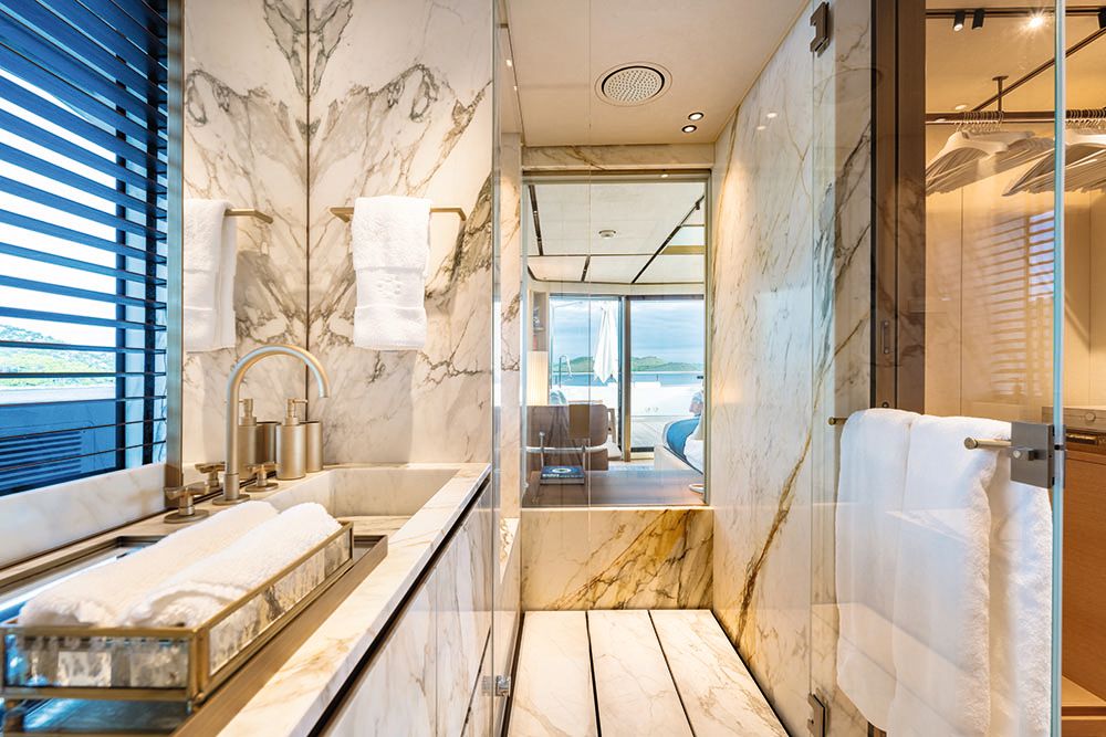 Interior of the bathroom, which is glass and white marble with dark veining. All the hardware is brushed metal and the towels are white