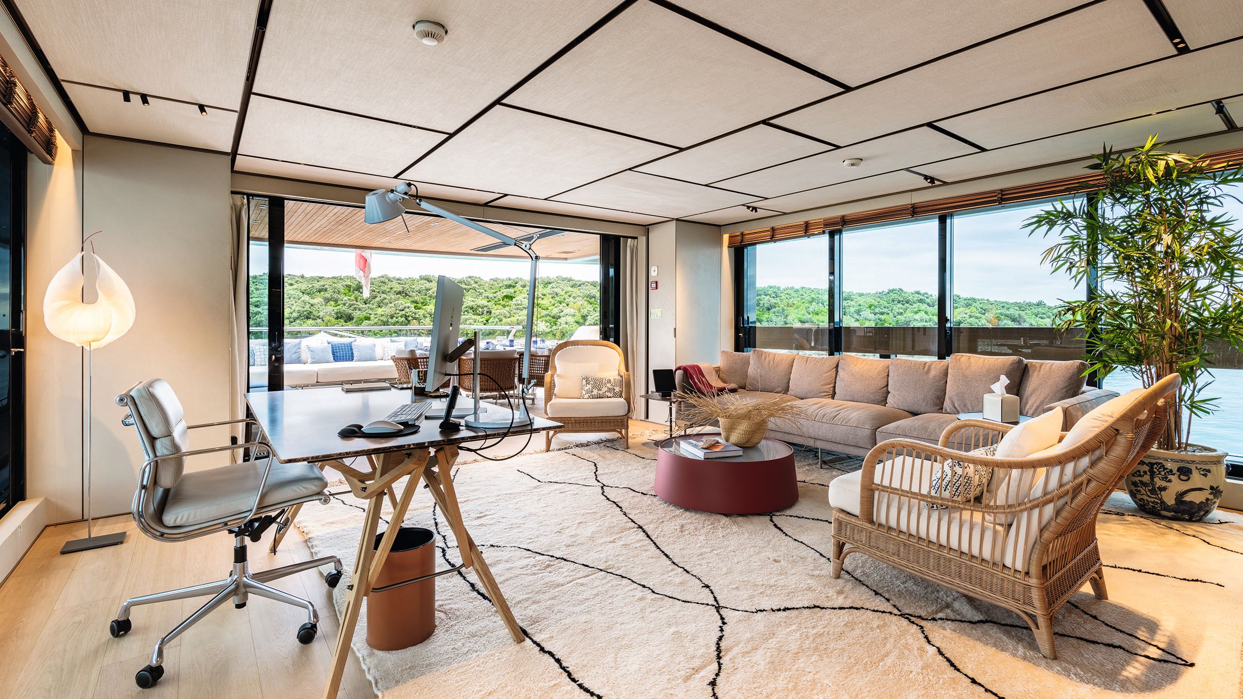 Large airy office space - a glass table with chair and anglepoise lamp faces into the room. Opposite is a sofa and wicker arm chairs. To the left are bifolding doors and to the front, the wall is entirely window