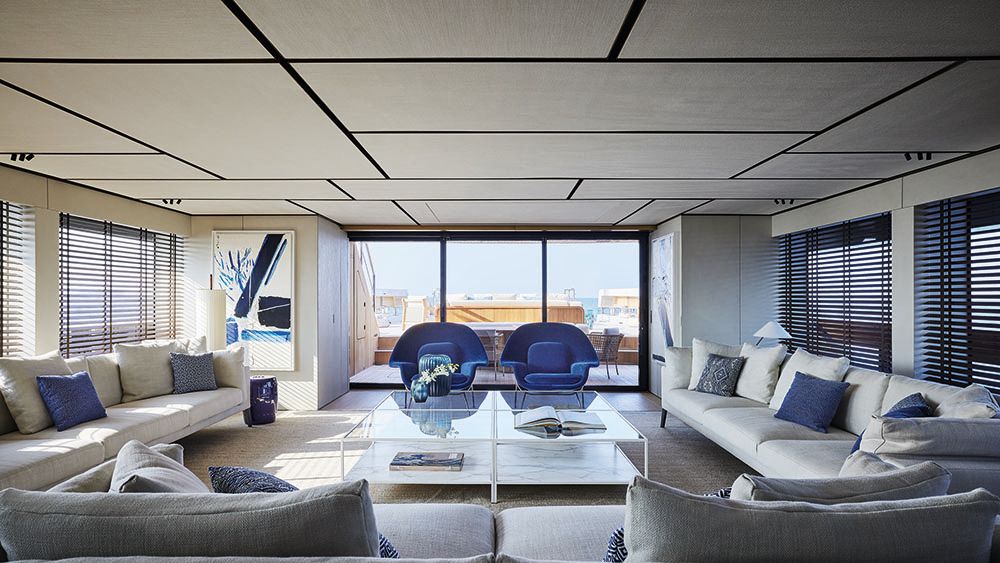 Large loung area with sofas and chairs arranged in a square around a large white and glass table. The colour scheme is white and blue
