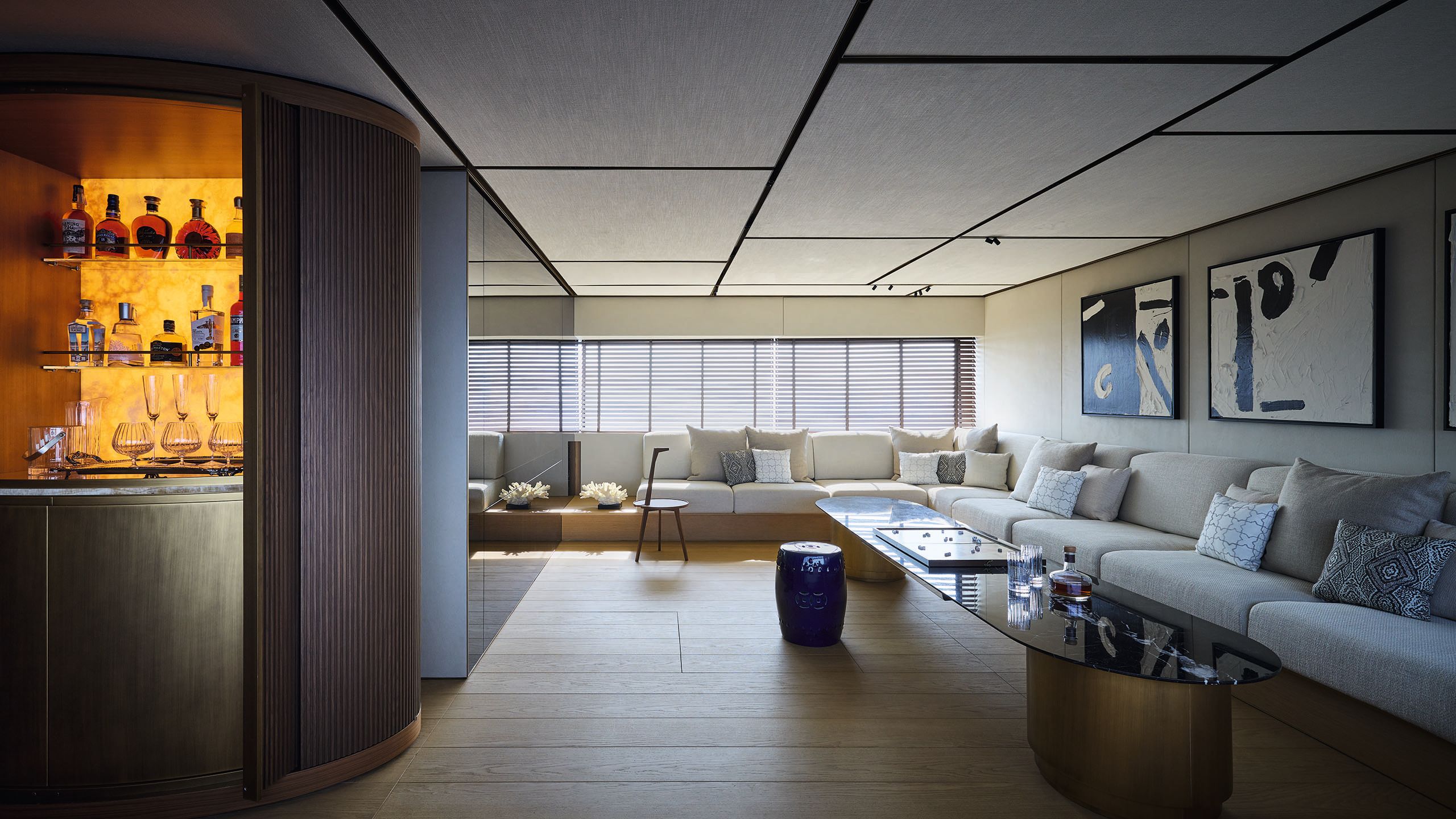 Looking into the media lounge which has L-shaped white sofas across the back wall and side. Low tables are in front of them and a bar area to the left