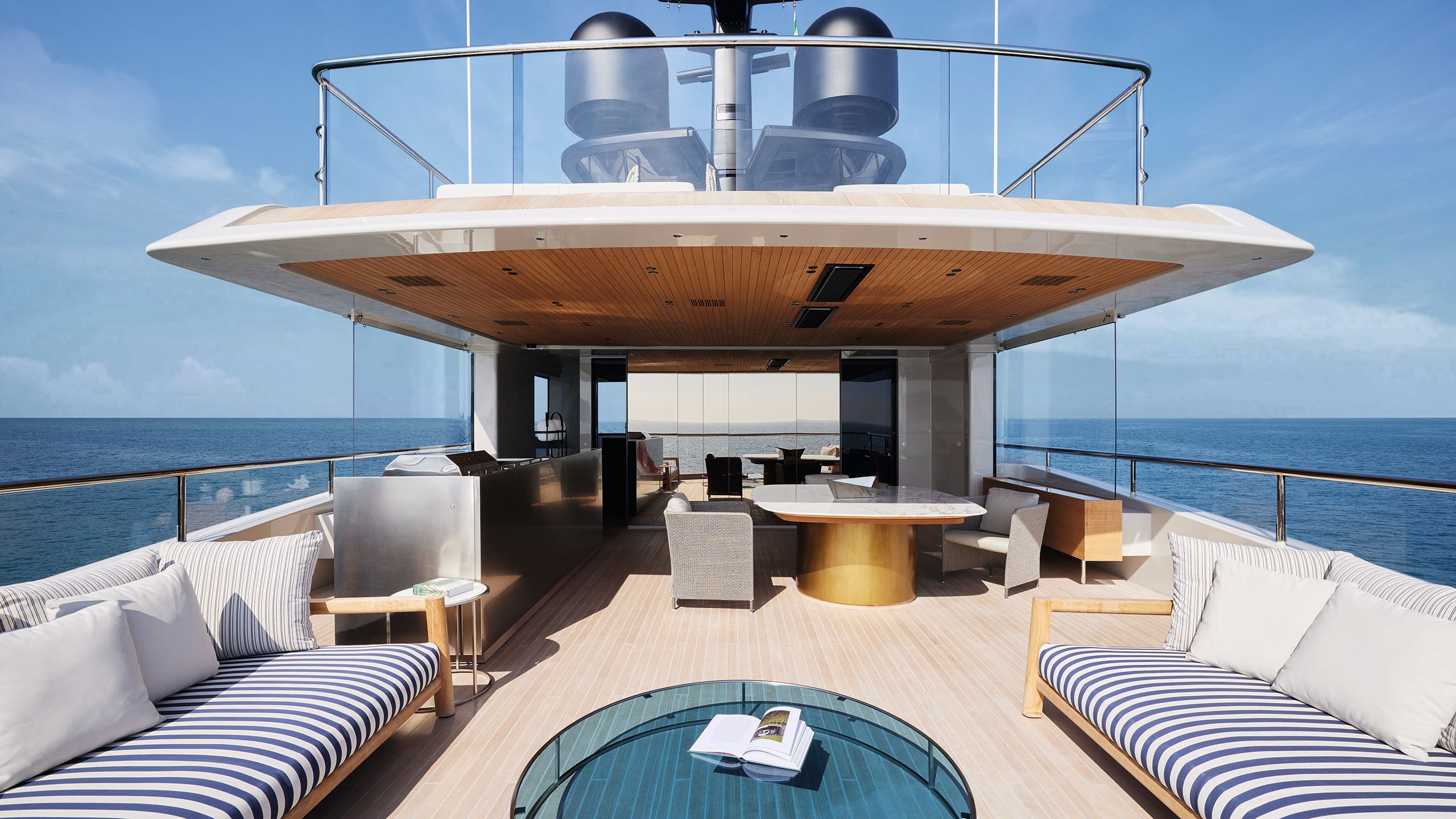 Partially covered outdoor deck area. Two sofas face each other with blue and white striped seat pads and a table between them. At the back is a dining table and chairs