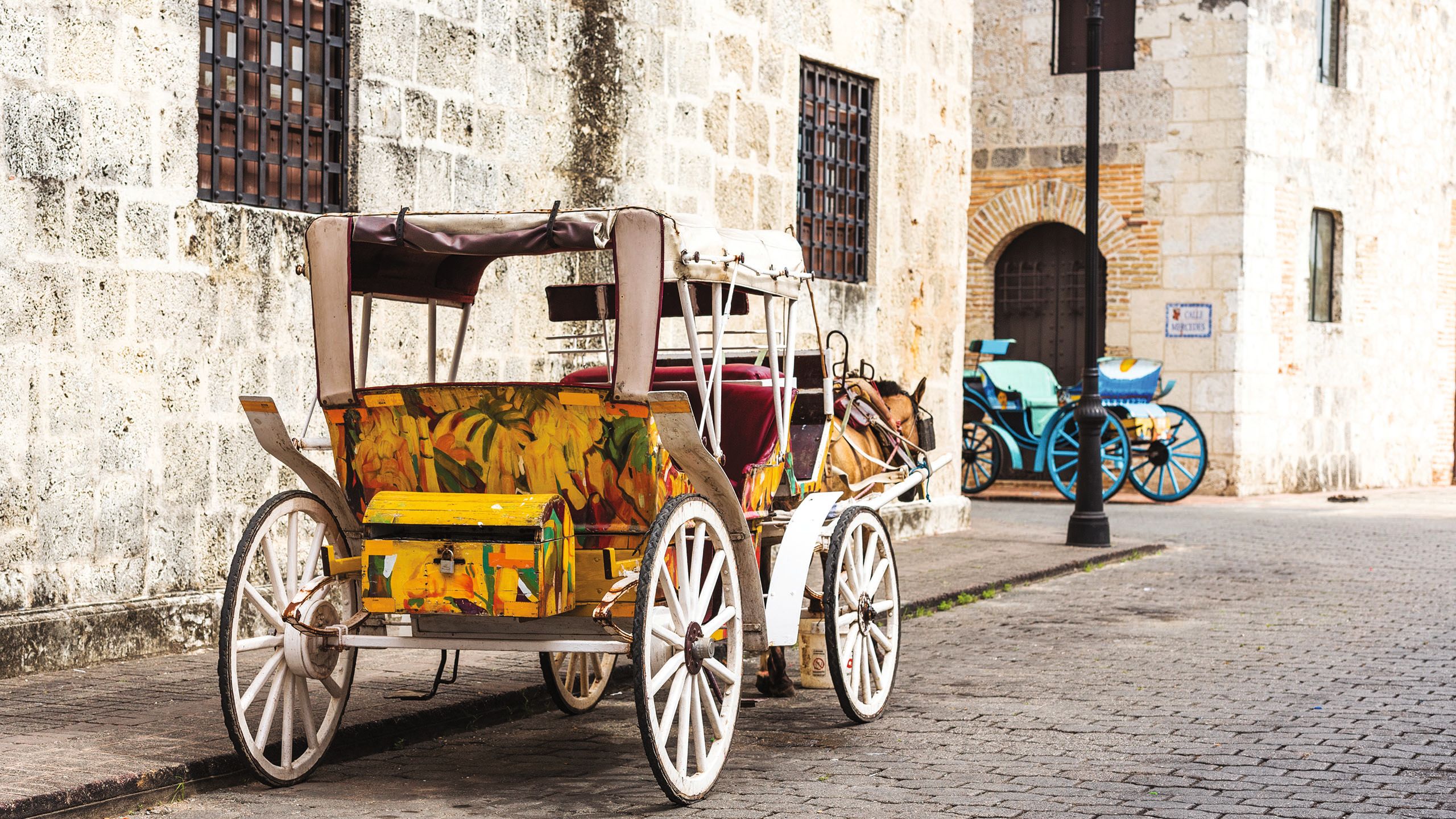 A white carriage with colourful orange and yellow seating, parked at the side of a cobbled street