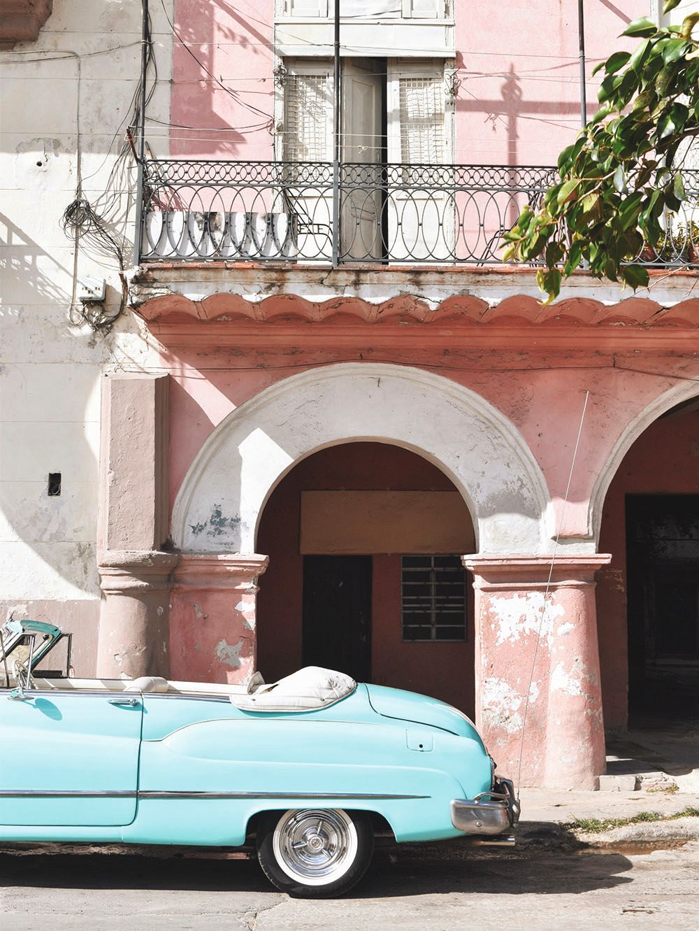 A pink building in Cuba with the rear portion of a vintage turquoise car with its roof down 