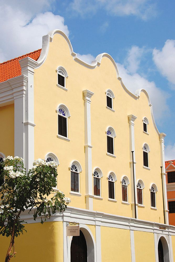 Colonial-style house painted yellow with an orange-tiled roof, white columns and trims around the roof and window arches 