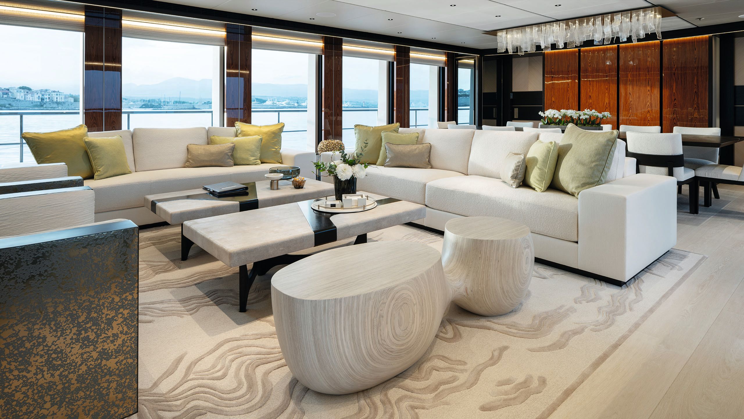 Two neutral coloured sofas arranged in an L with green scatter cushions, two arm chairs facing, two rectangular coffee tables in front and an abstract circular table in a neutral woodgrain effect to the side