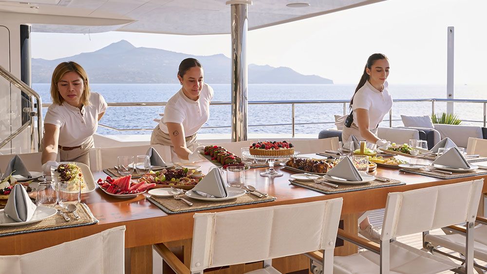Three female servers placing plates on a table full of gourmet food
