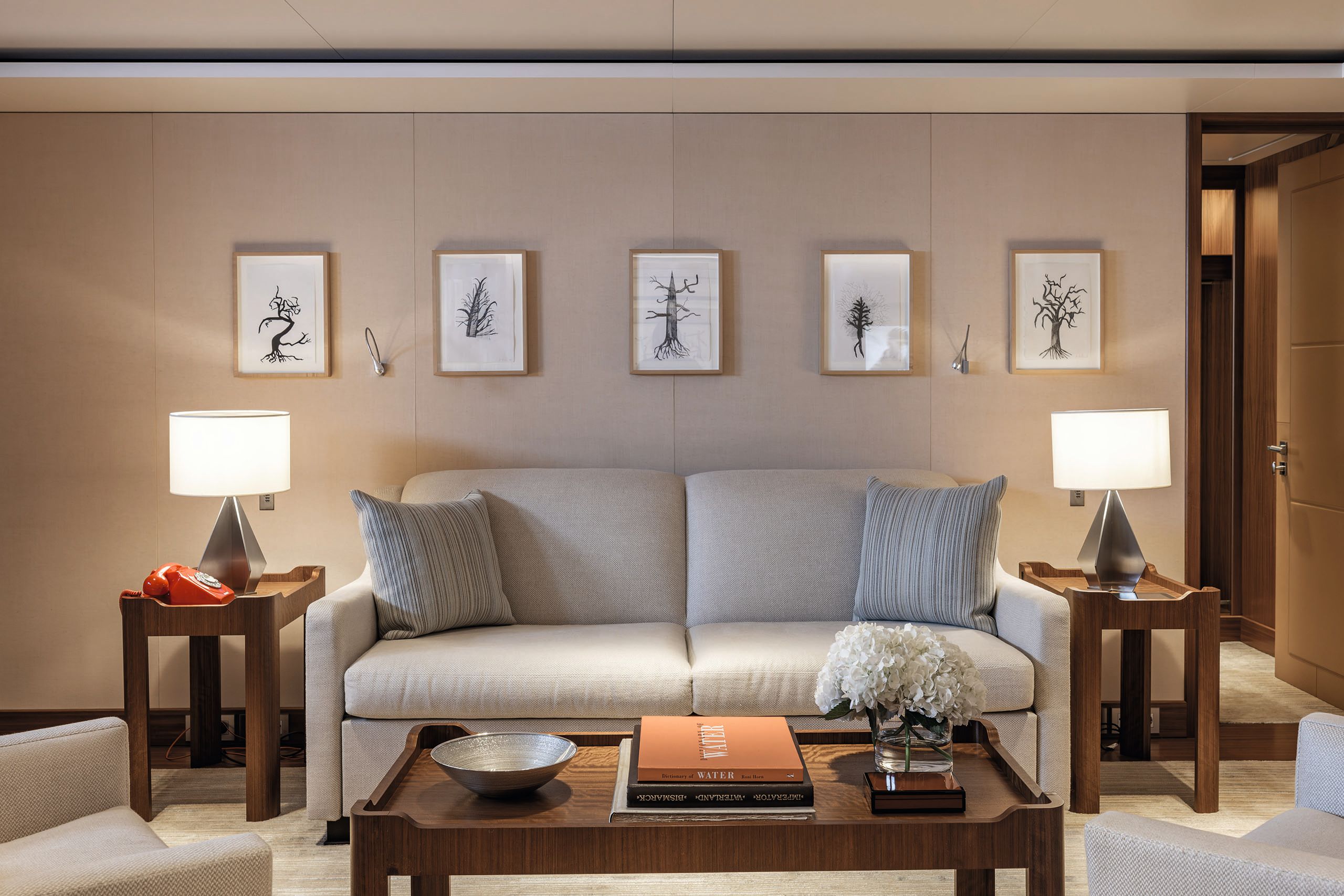 Front view of a cream sofa with wooden coffee table, two side tables with a lamp each, and five pictures on the wall behind