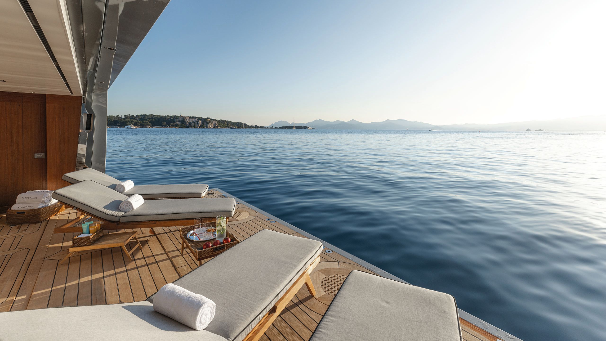 Four sun loungers, each with a rolled up towel on them, on the beach club area