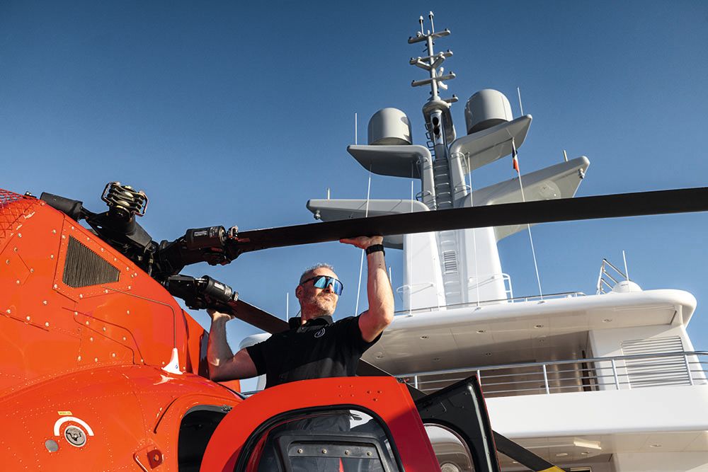 A man holding on to a blade of the helicopter's propeller, as shot from below
