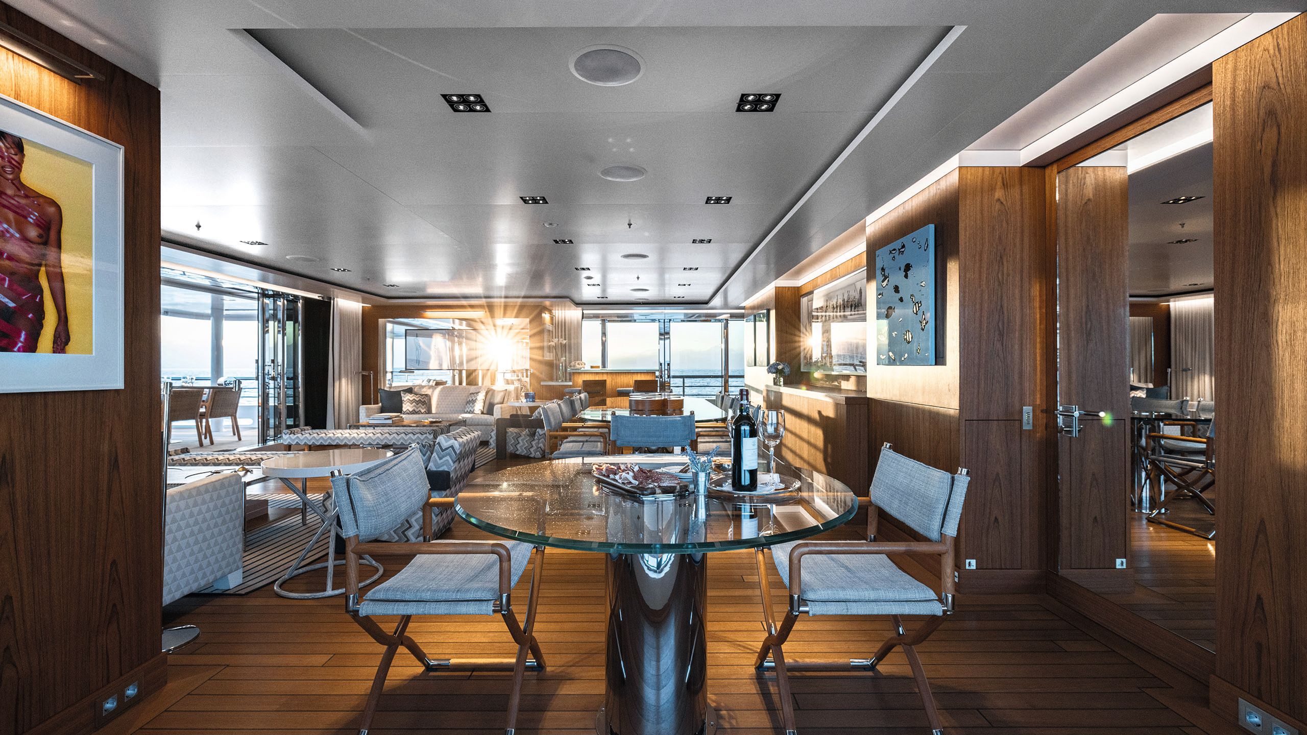 Long view of the lounge area which has wooden floors, a glass round table and three chairs, soft seating and wood features along the walls