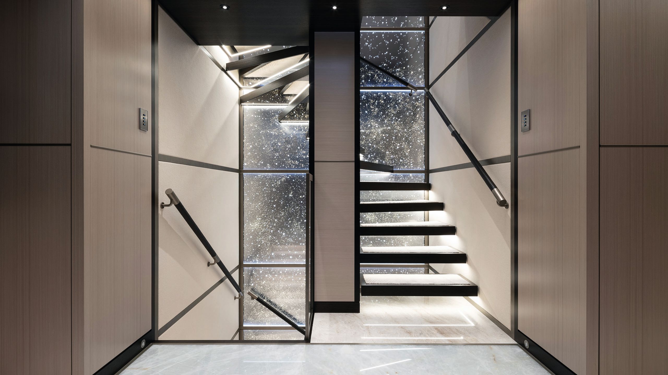Wide shot of the staircase which has treads lit from underneath. The glass behind is frosted and speckled