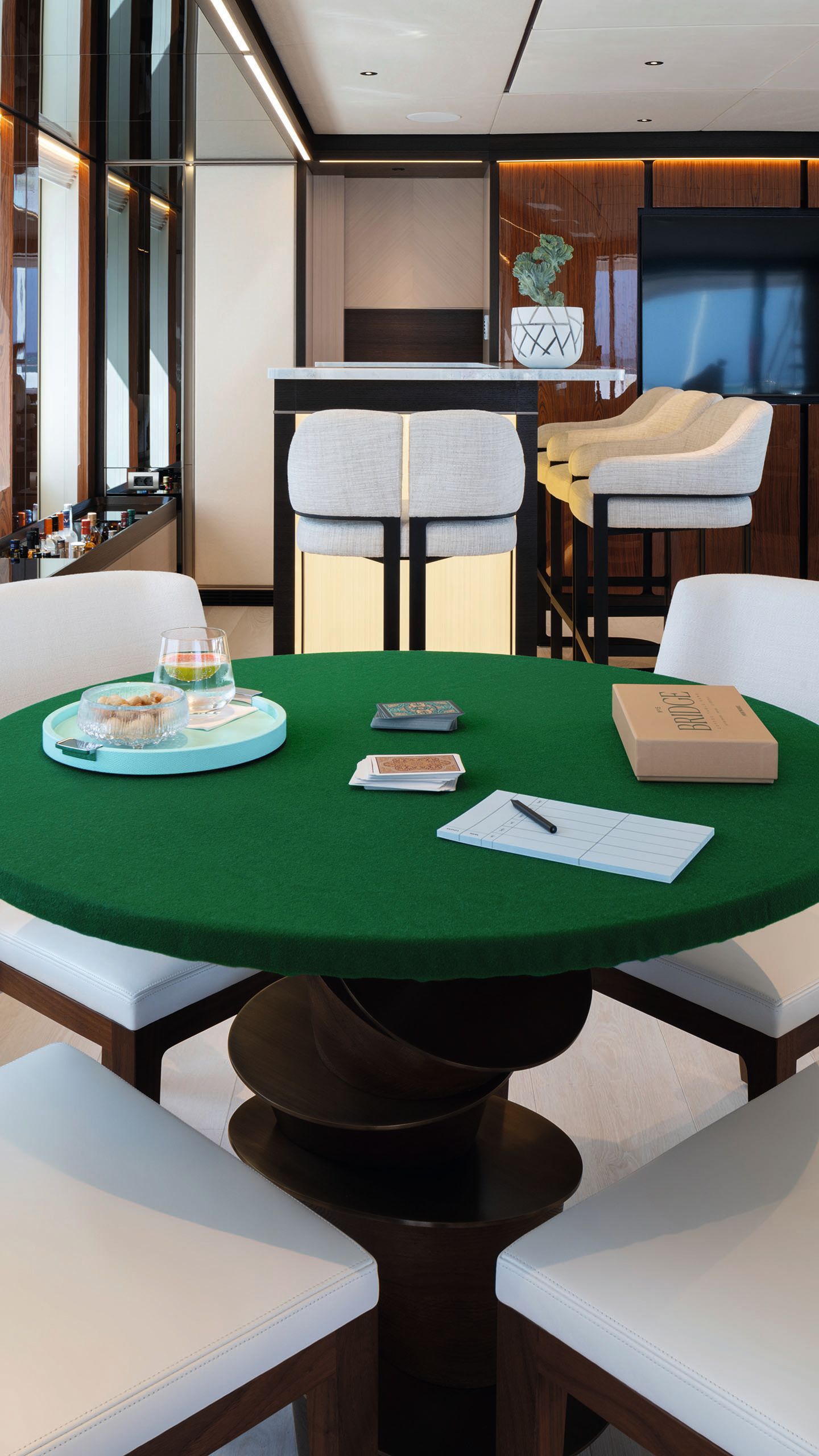 A round games table with green felt top. There are games, a notepad and drink on top