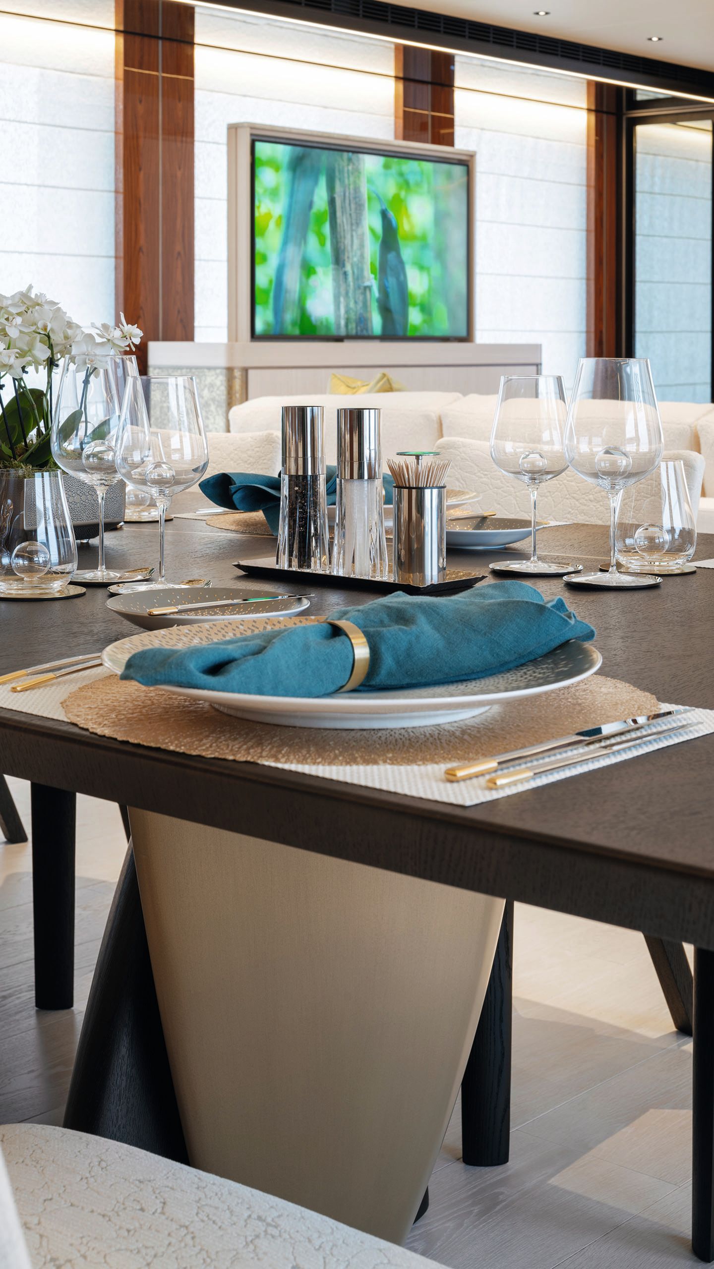 A mahogany coloured table with place setting including plate, napkin in a ring, cutlery and wine glasses