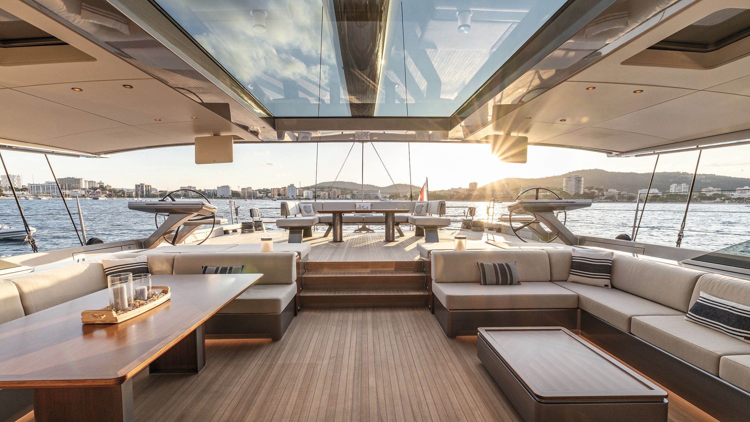 Covered deck area looking out towards the water. Each side has L-shaped banquette seating - the left has a large dining-style table and the right has a low coffee table