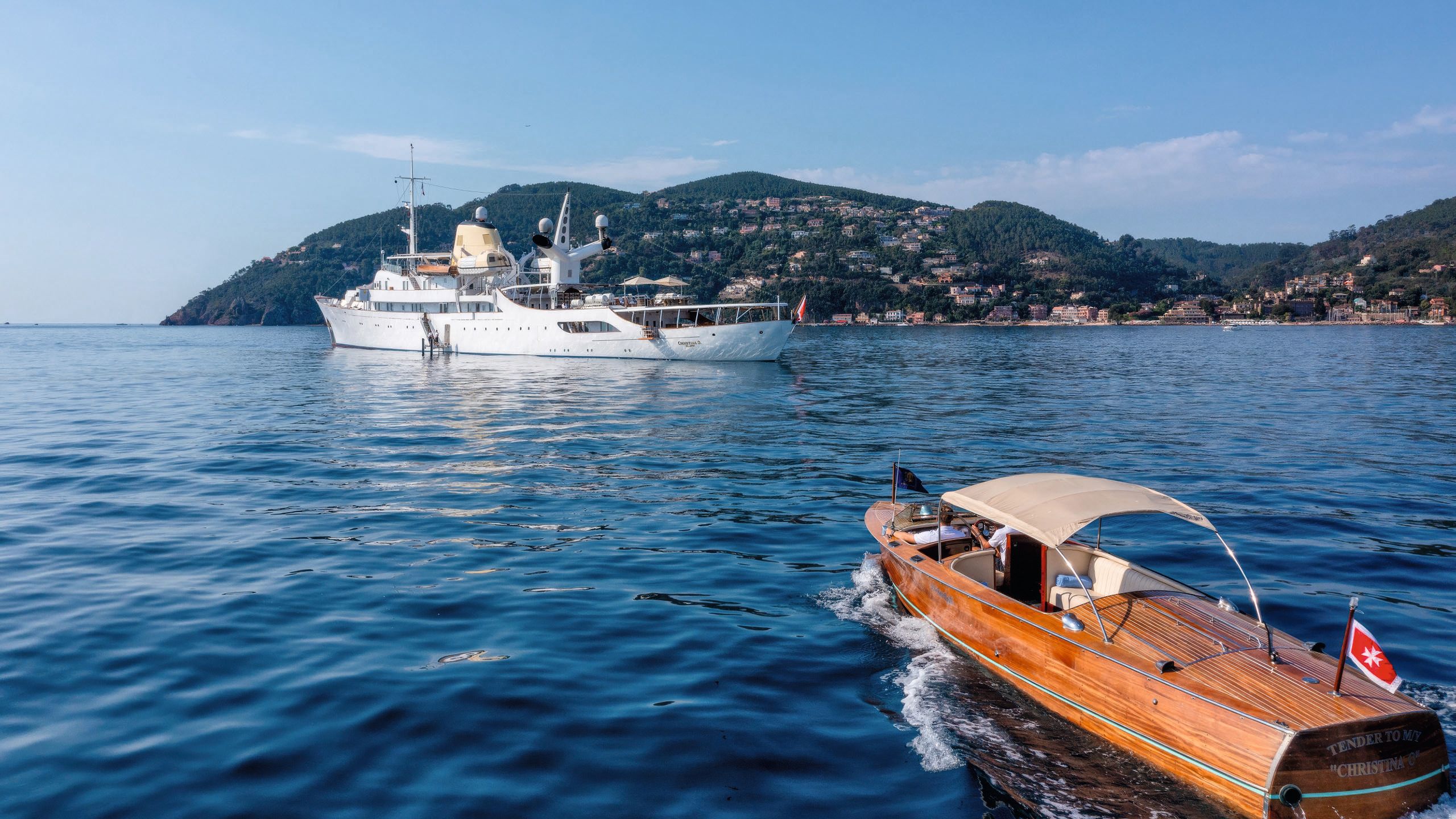 A side view of Christina O in the background. In the foreground is one of its teak-coloured tenders