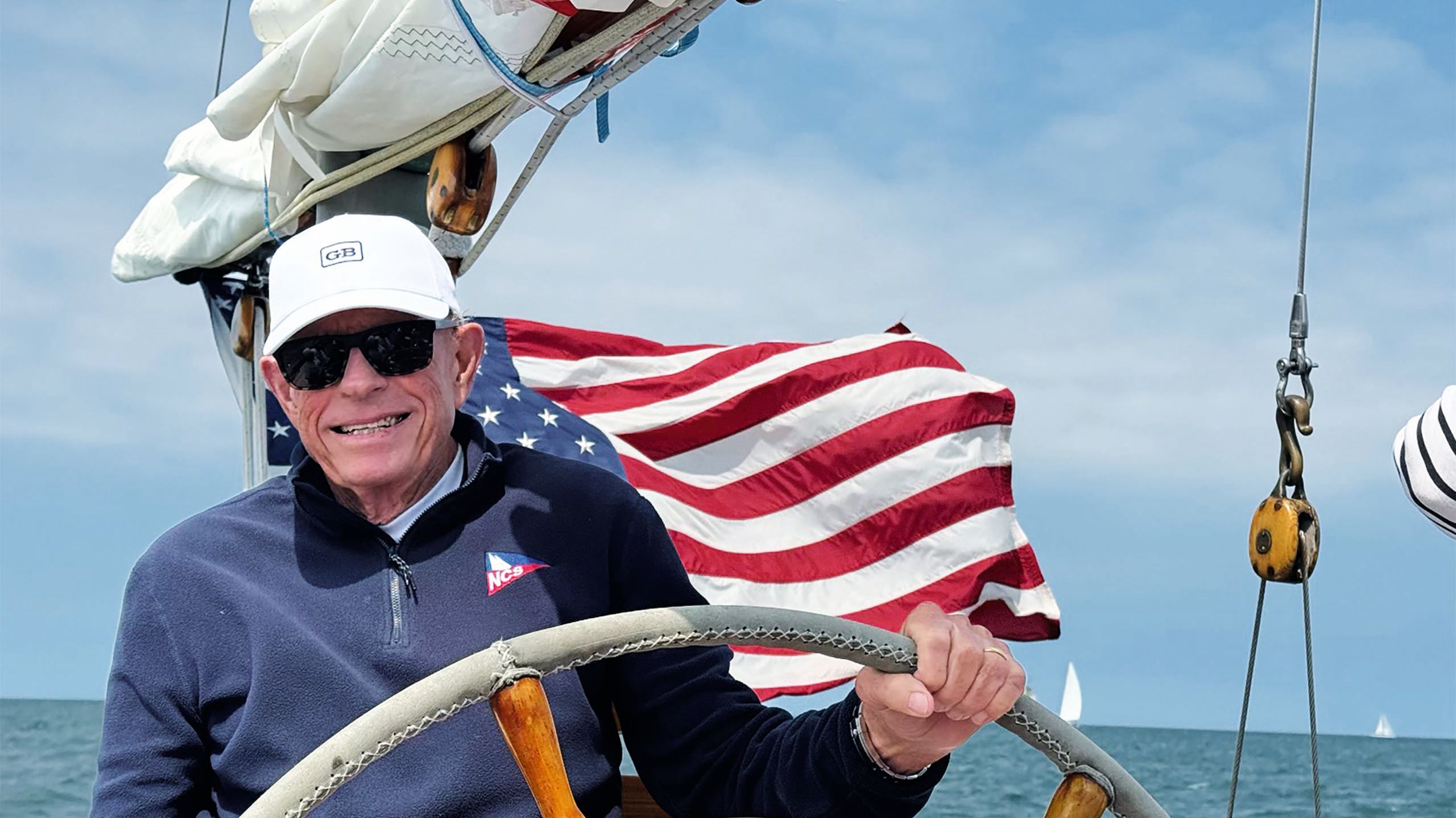 Tom Whidden at the wheel of a vessel with a US flag billowing behind