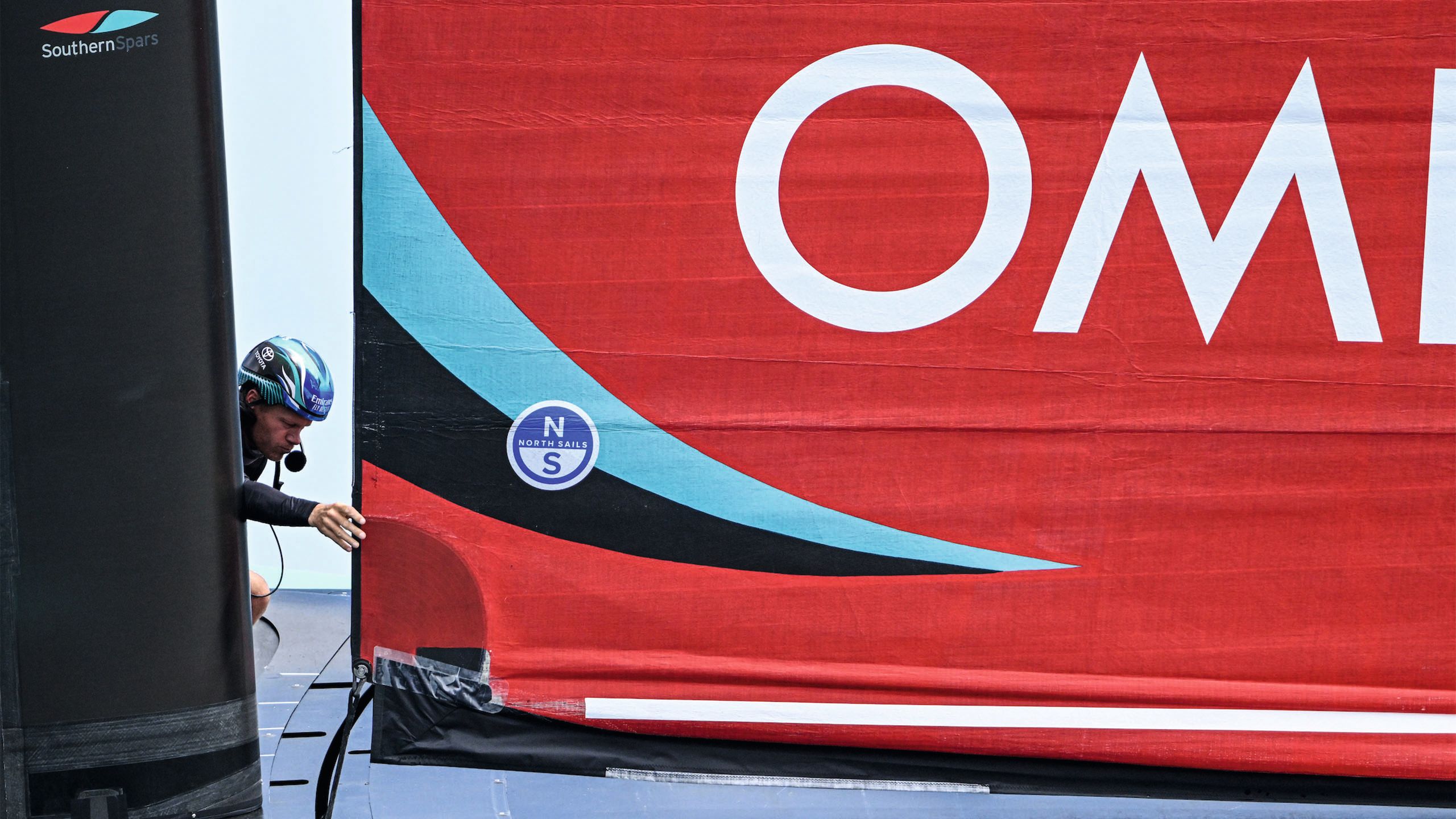 Close-up of a red, blue and black sail with white writing on it - a man is holding the edge of the sail