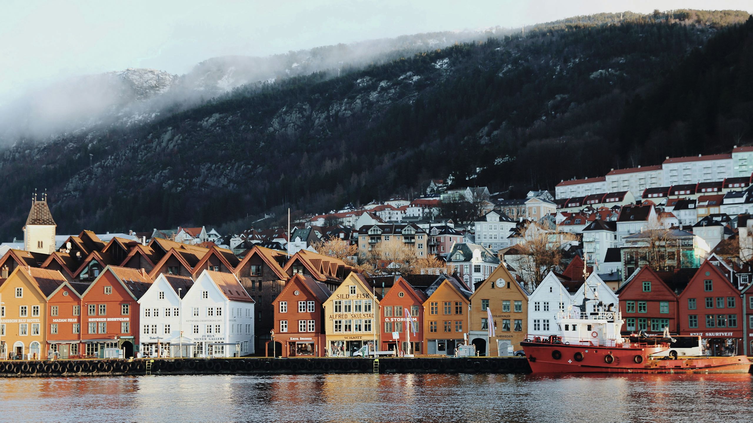 Colourful houses in Norway along the shoreline, with misty mountains in the backround
