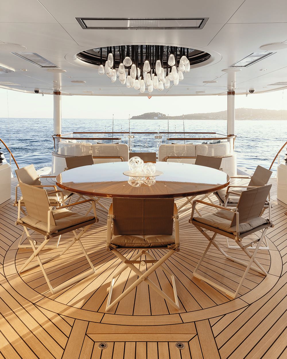 Outdoor, covered seating area with circular table and seating for eight. There is an abstract glass chandelier above with individual pendant lights