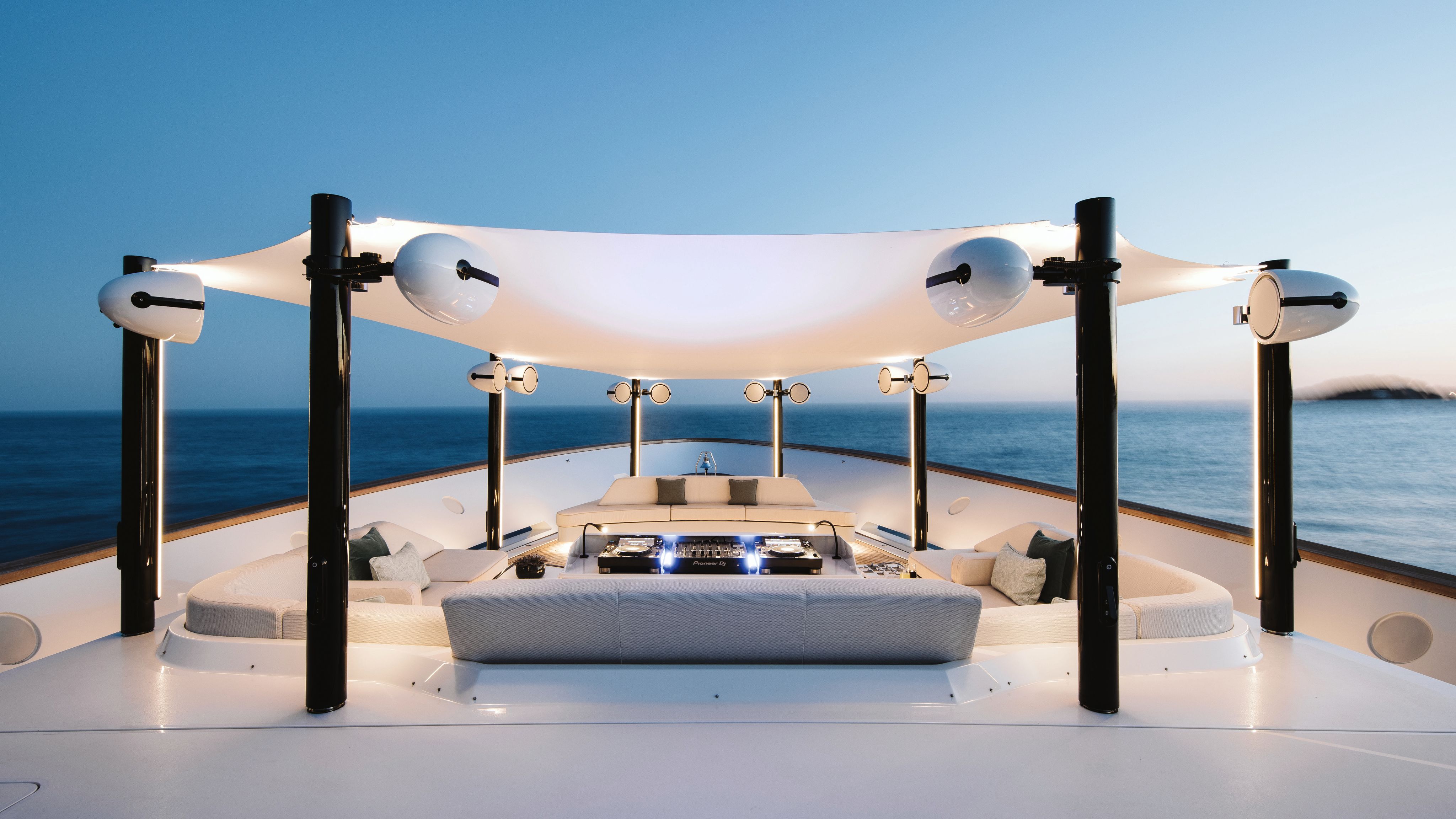 Outdoor decking area with large soft seating and white speakers on black poles surrounding them