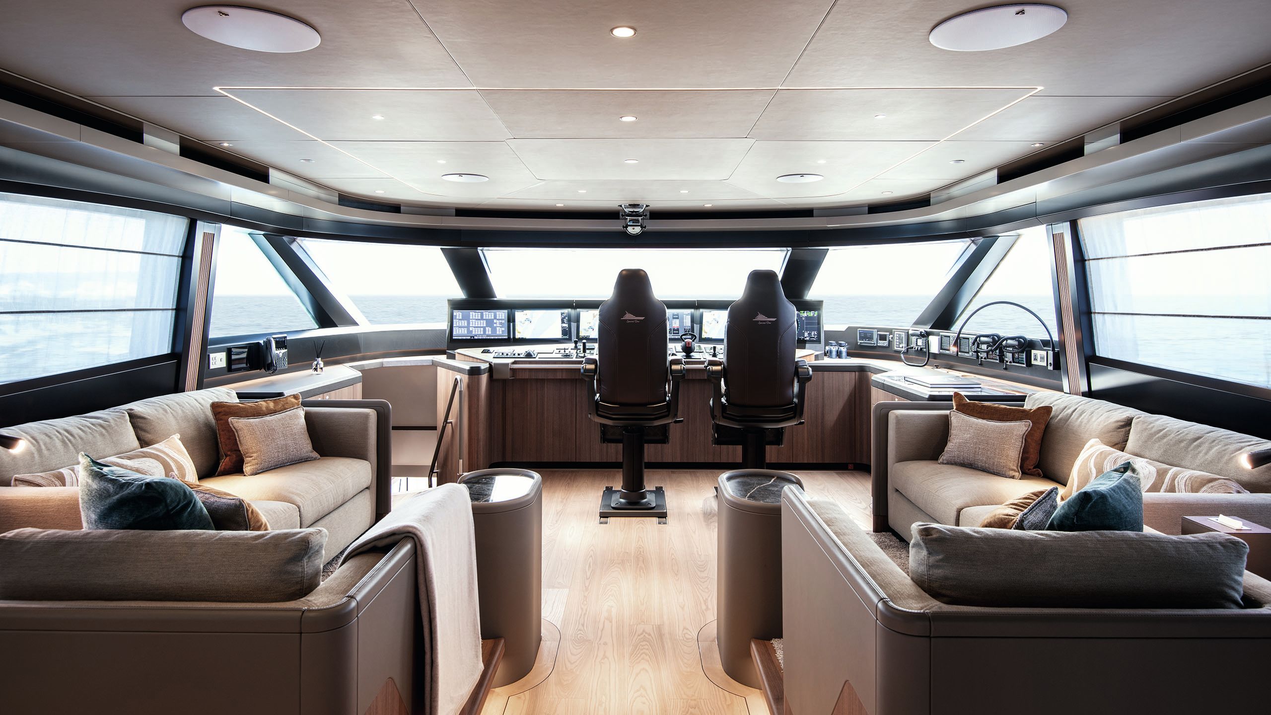 Interior of the bridge, featuring two brown and cream L-shape sofas and two large black leather chairs to the front of the vessel, overlooking a control panel 
