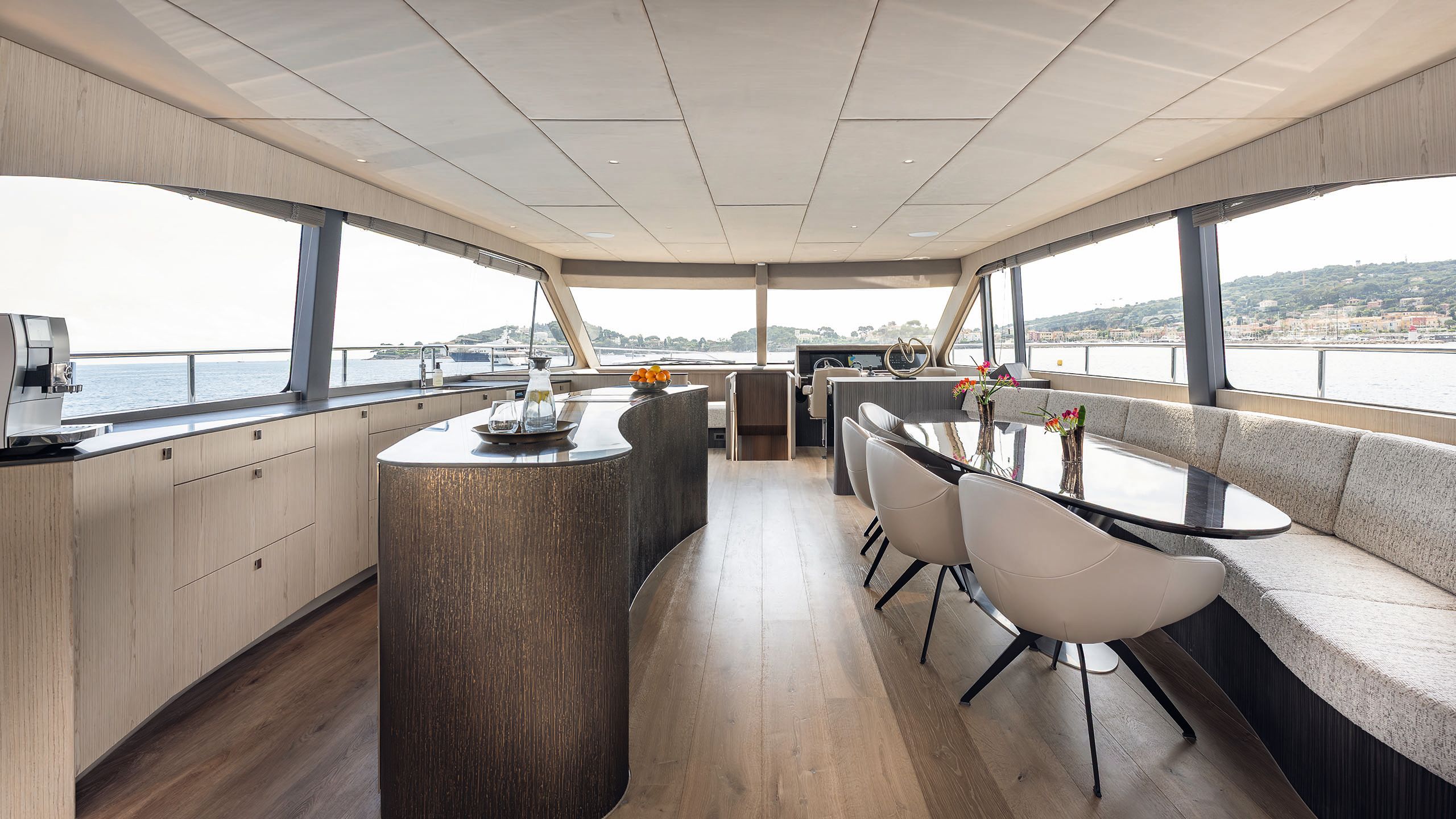 Kidney-shaped kitchen island opposite counters on the left; on the right is soft banquette seating and a black glossy dining table with grey chairs
