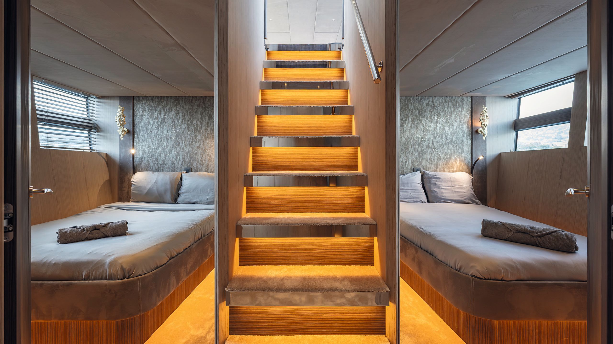 Looking up a staircase from the guest cabins. The staircase is central and has treads lit from underneath, making them look orange. There is a double bed either side
