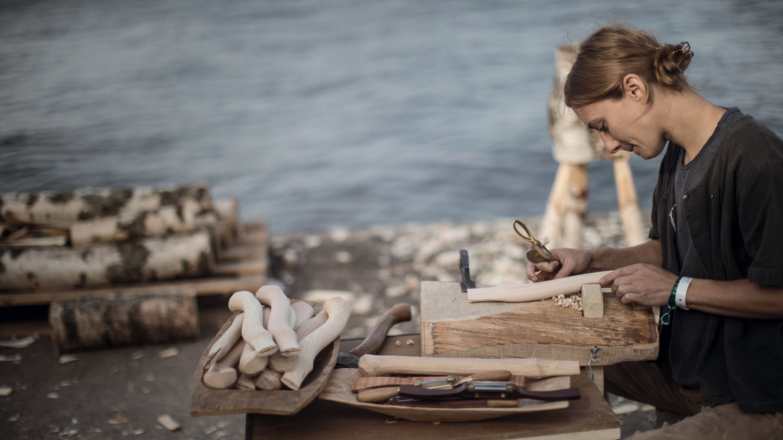 A woman sitting outside and whittling or carving into some wood 