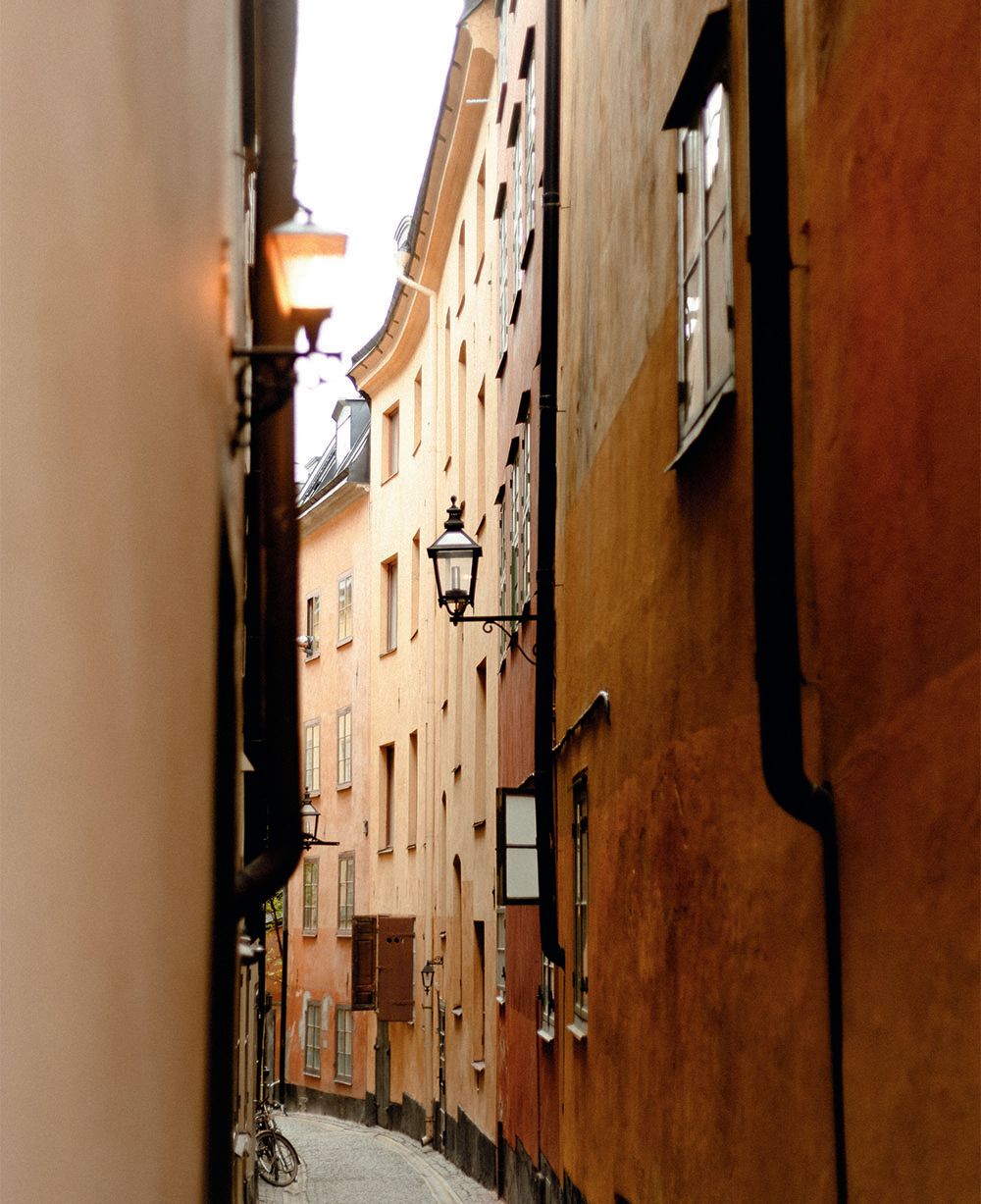 Looking down a side street; the buildings are a pale orange and there are old-style gas streetlights