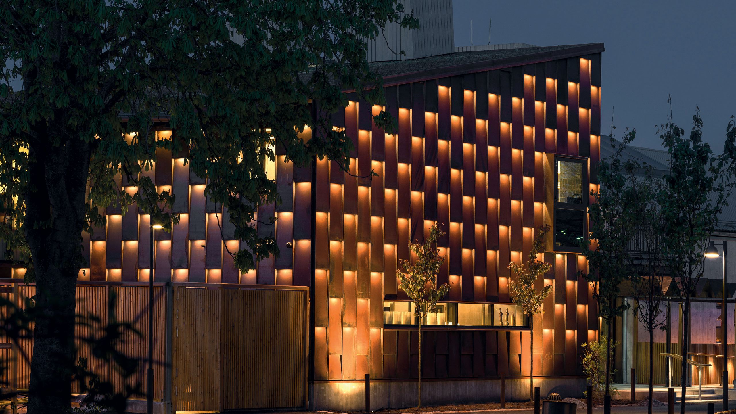 Exterior view of a building at night covered in squares which are individually lit in orange
