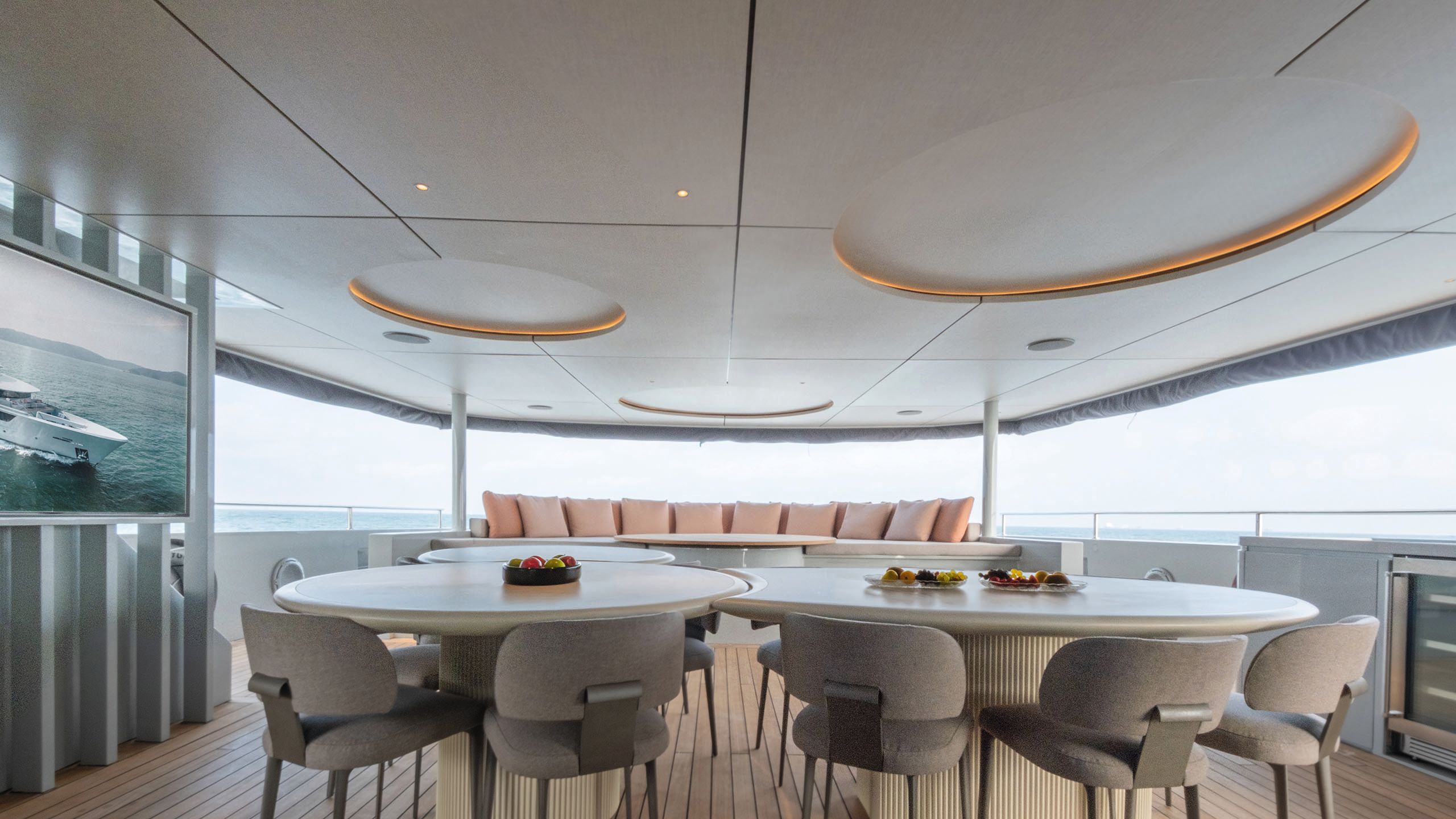 Covered exterior dining area with two circular tables for eating at and a large curved pink sofa in the background