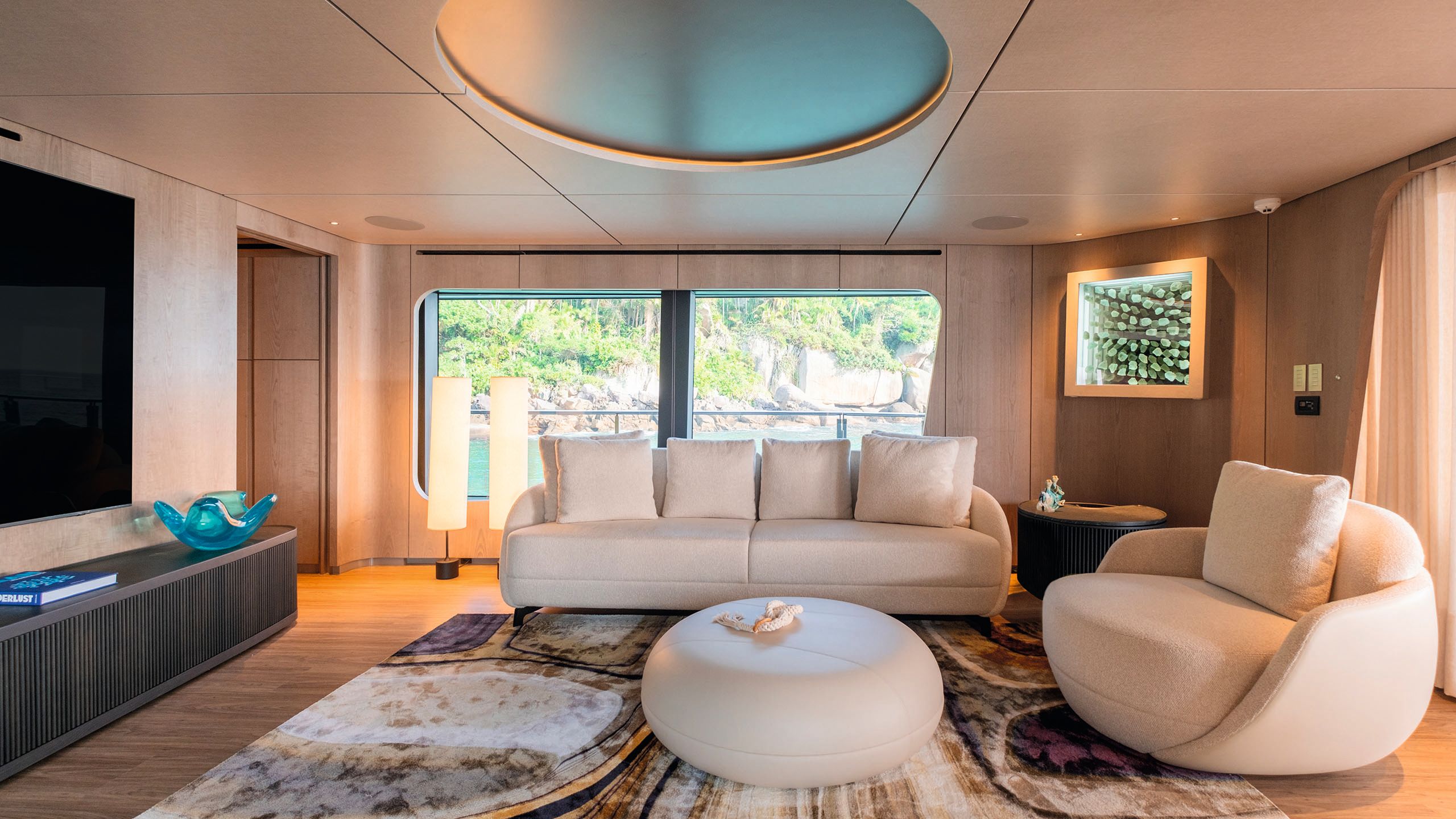 TV room with large screen on the wall. There is a small cream sofa, armchair and table facing it. The walls are wood panelled in a light colour and there are turquoise accents throughout