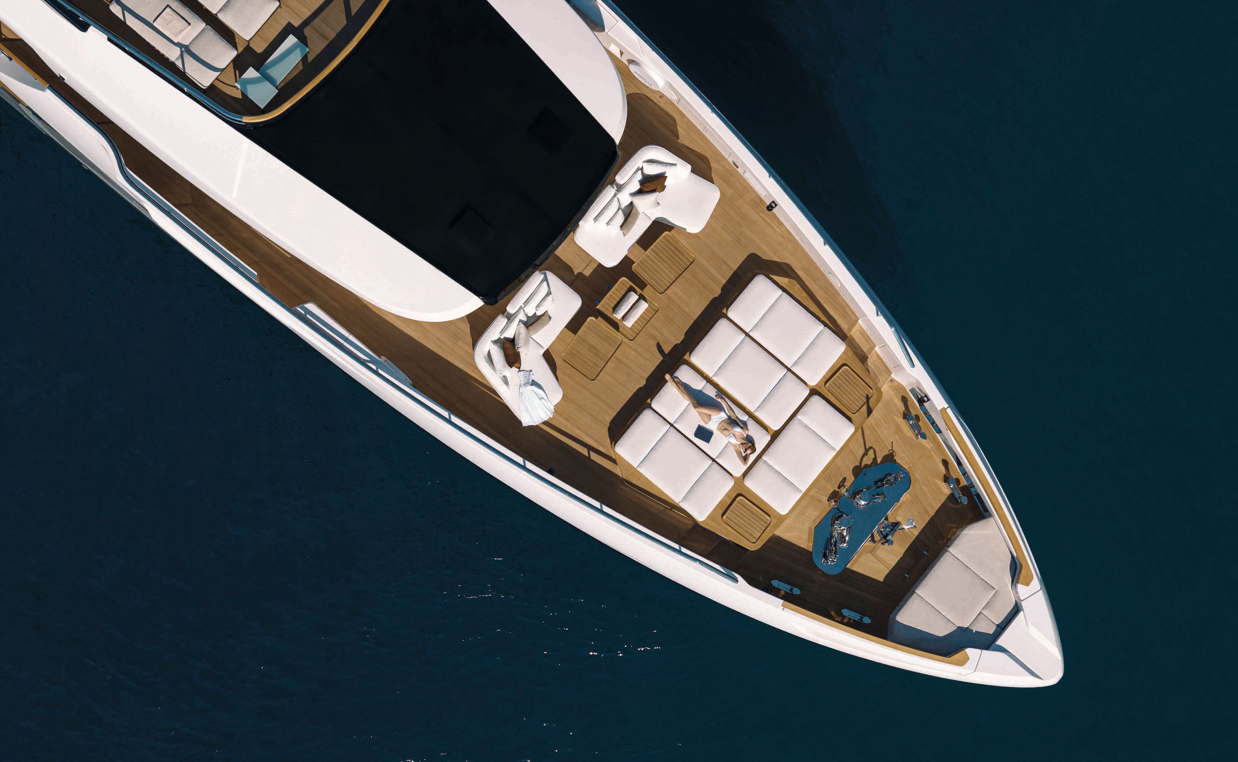 Overhead view of the tip of a Custom Line boat. There is a large white sunpad in the centre and white chairs towards the back