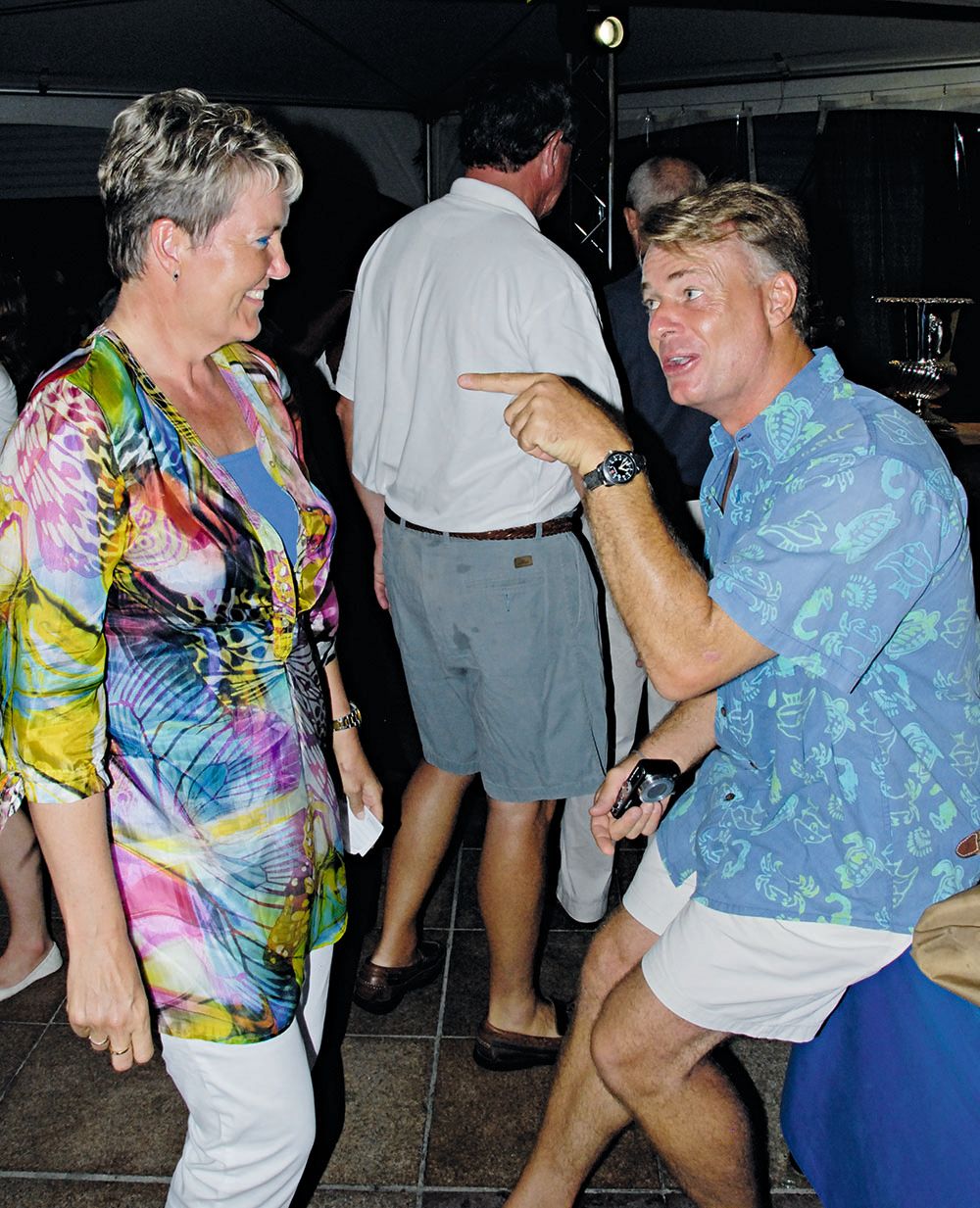 A man and a woman at a party - the man is pointing at her and she is smiling