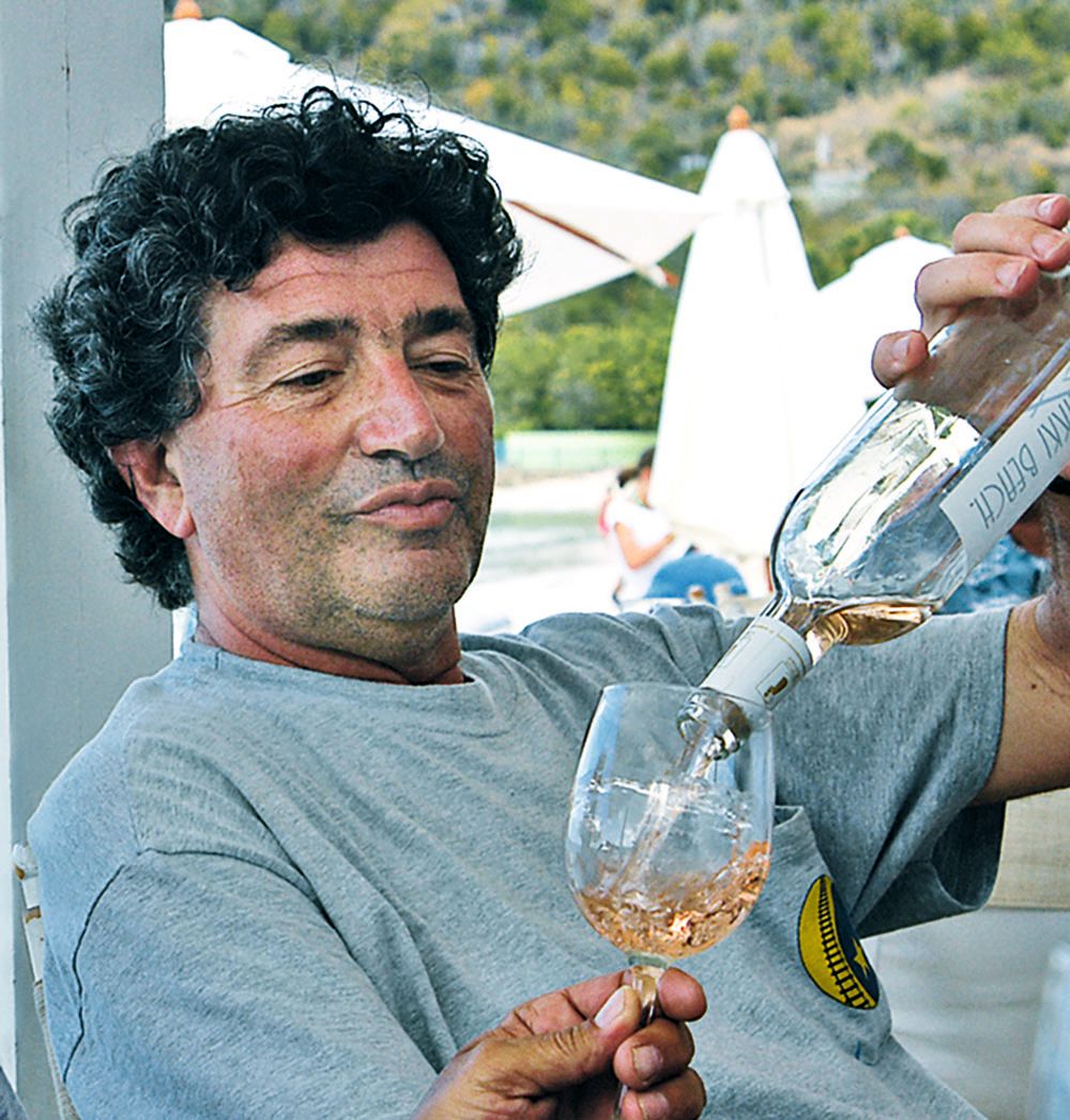 A man with curly black hair is pouring rose wine into a glass