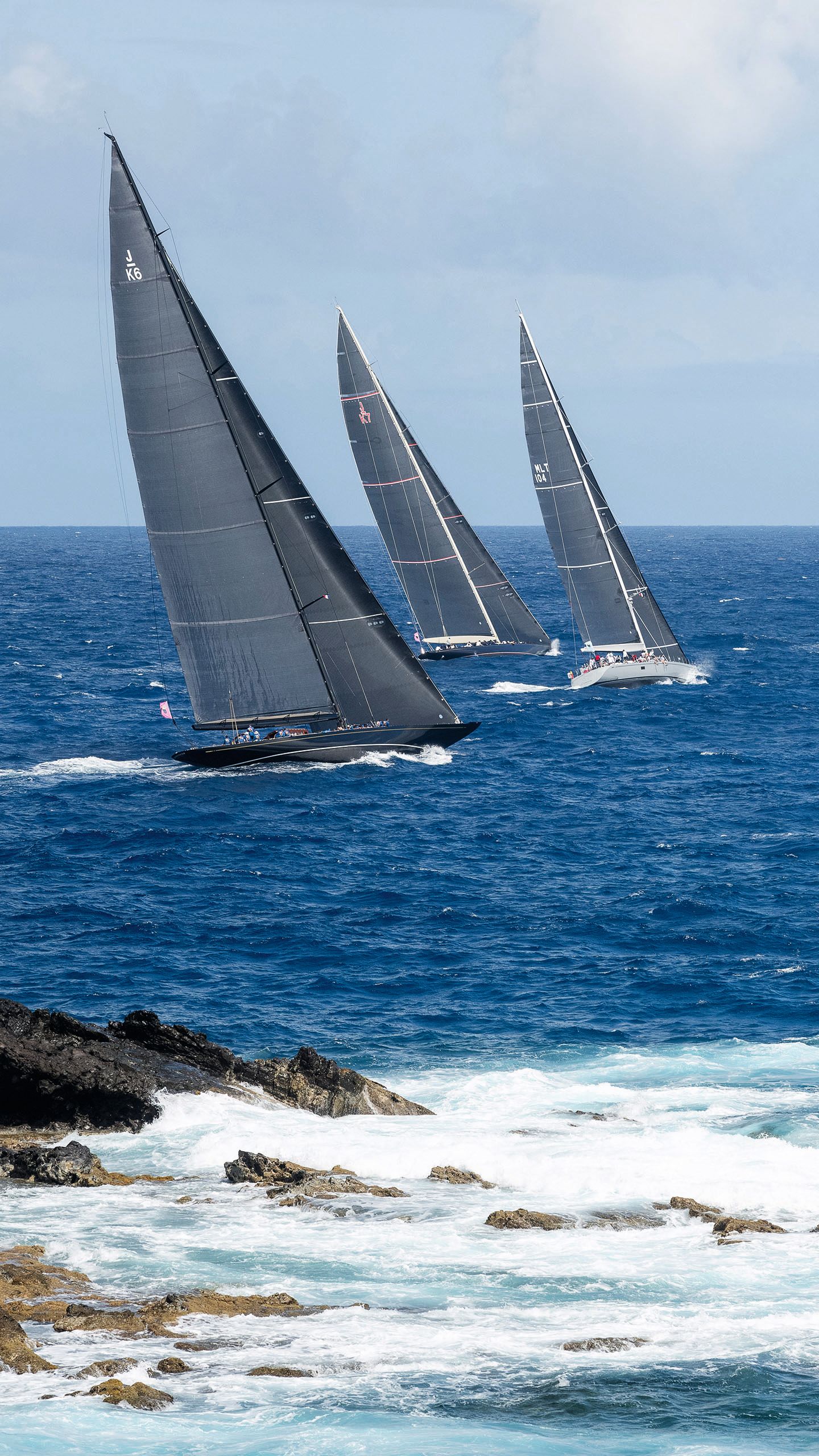 Three sail boats on the water - they each have large grey sails