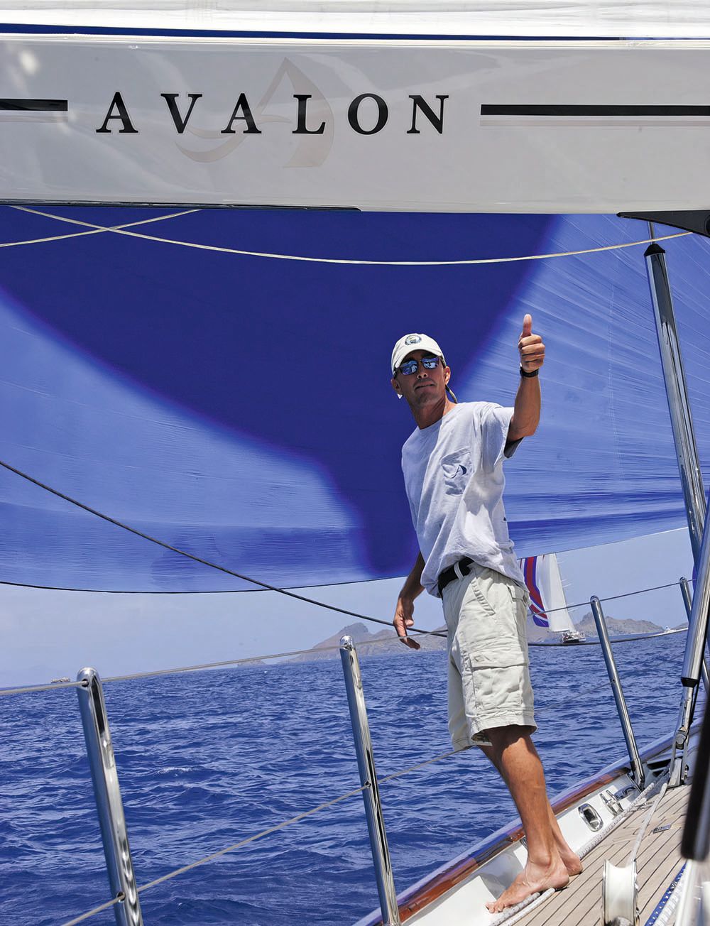 A barefoot man standing on the deck of the Avalon. He is raising a thumbs up