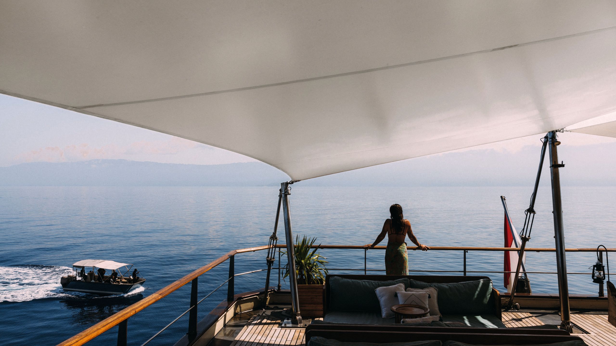A woman with her back to the camera, standing on the deck of a boat with her hands on her handrail
