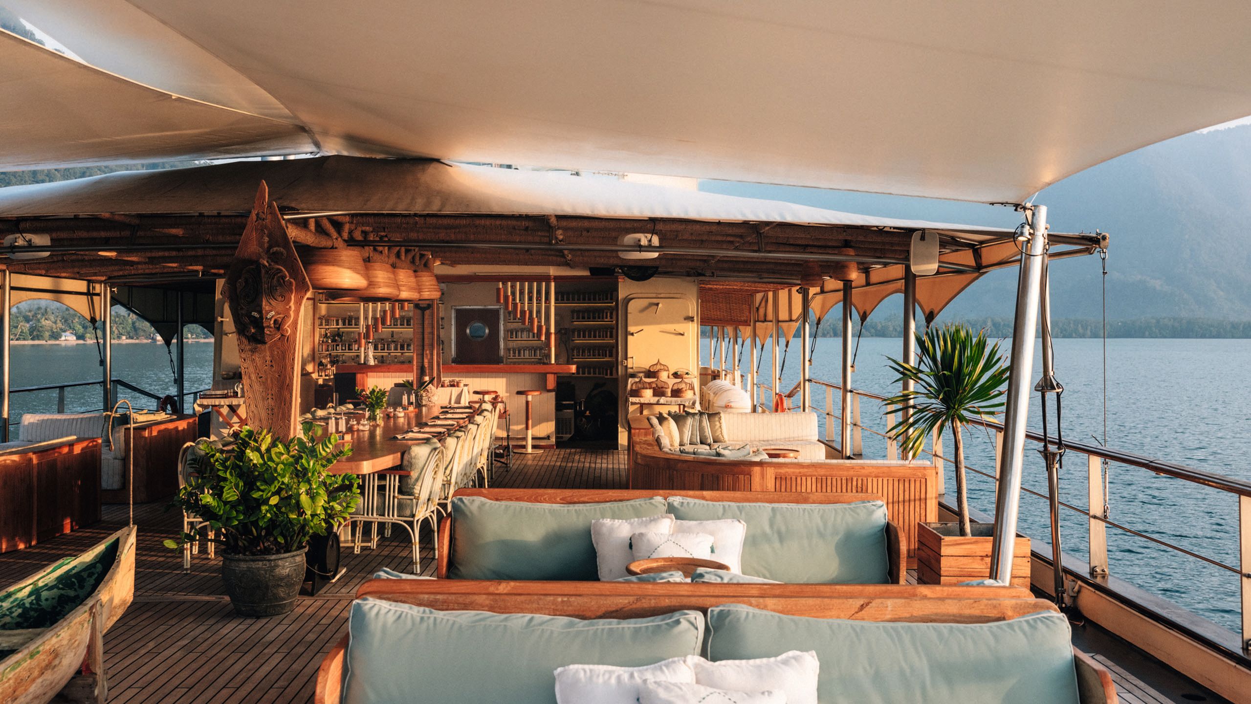 An outdoor covered seating area with large dining table running down the middle and bar in the background