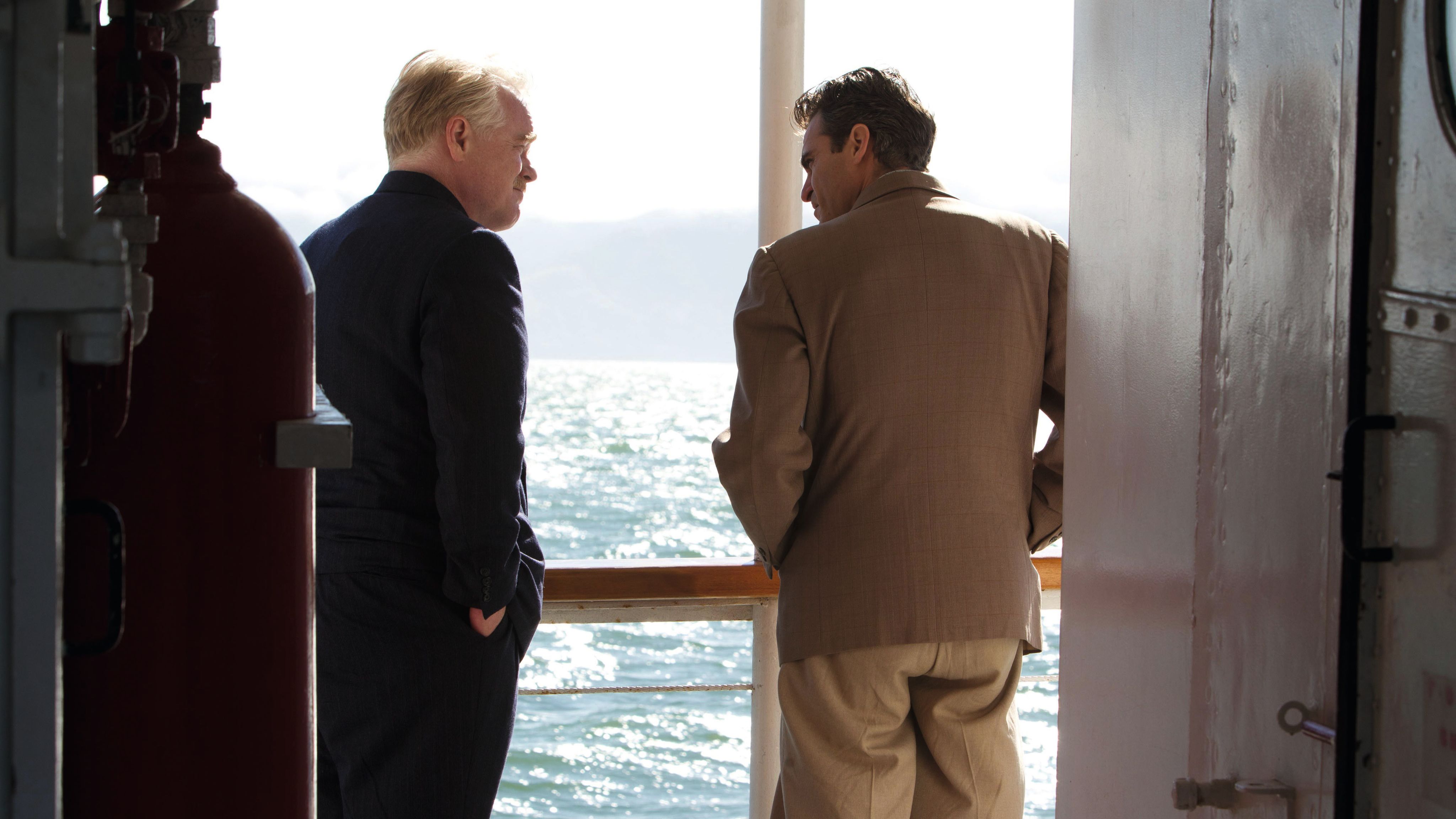 Hoffman and Phoenix as photographed from the back, standing on the deck with their hands in their pockets. Both are wearing smart jackets